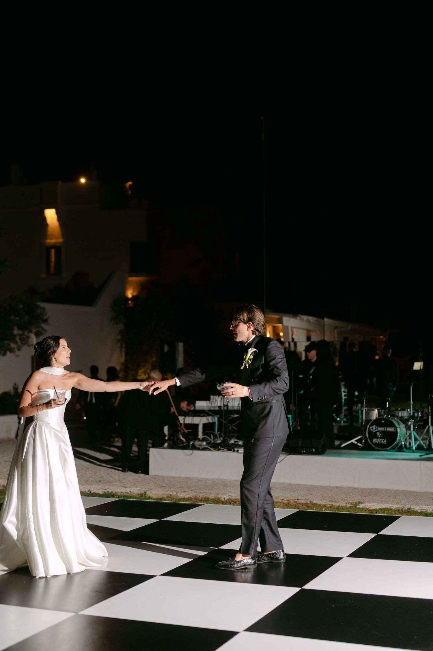 Bride and groom share first dance on black and white checkered outdoor dance floor at night.