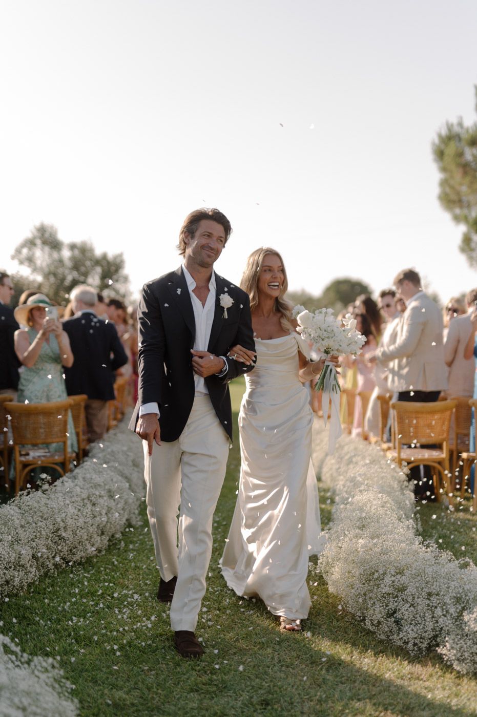 Wedding party walks through a field of white flowers at sunset.