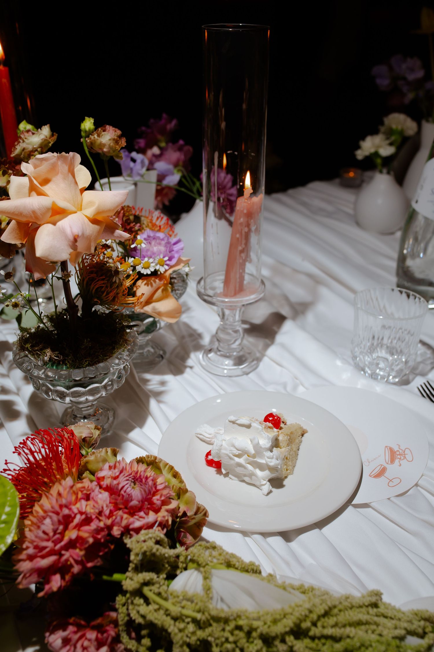 Elegant table setting with colorful flowers, candles and slice of wedding cake.