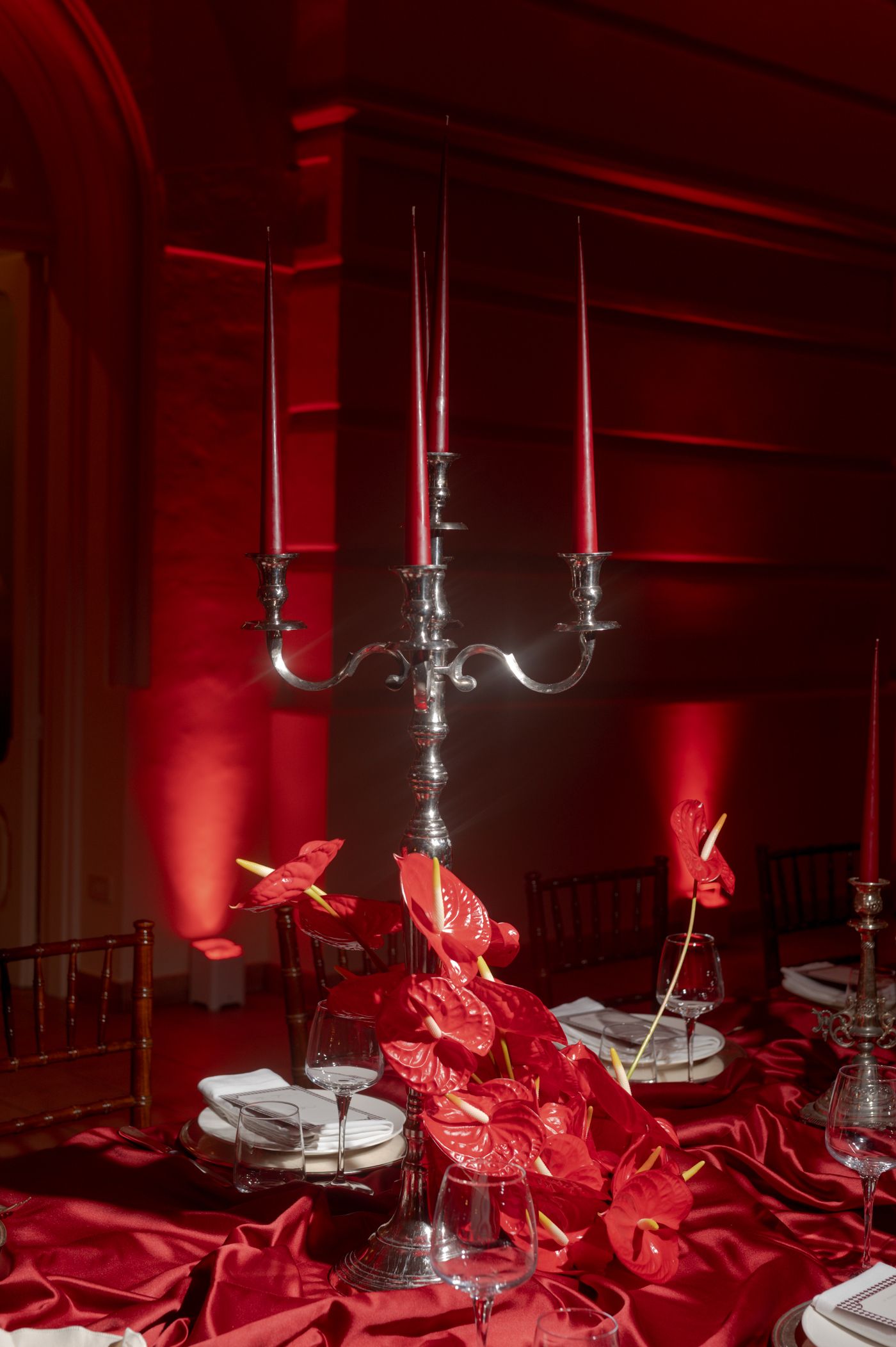 Red silk fabric draped elegantly on a table beneath hanging silver candelabras in a dimly lit room.