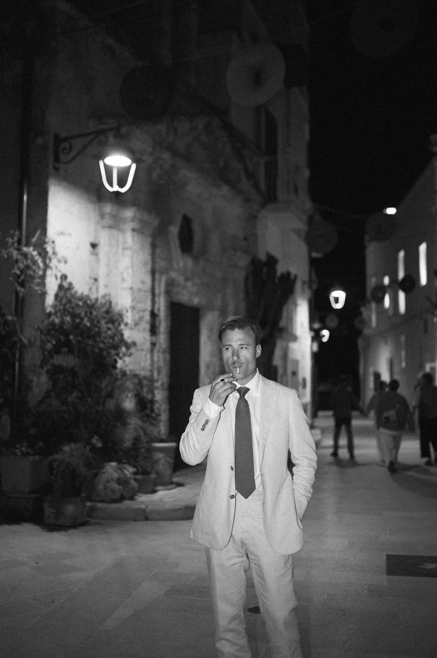 Black and white nighttime street scene with stone walls and glowing lanterns.
