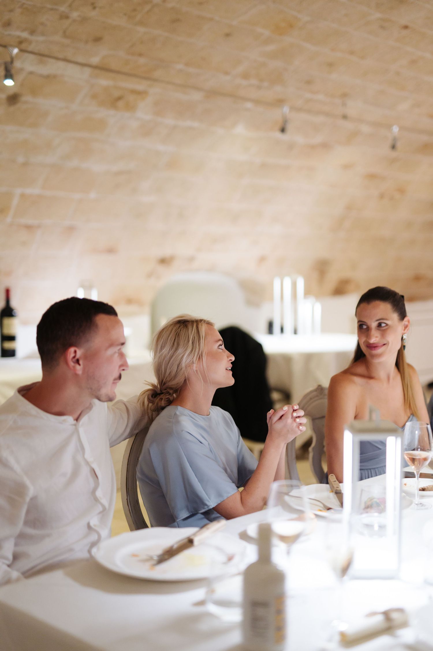 Wedding guests enjoying an elegant dinner reception in a bright stone-walled venue.