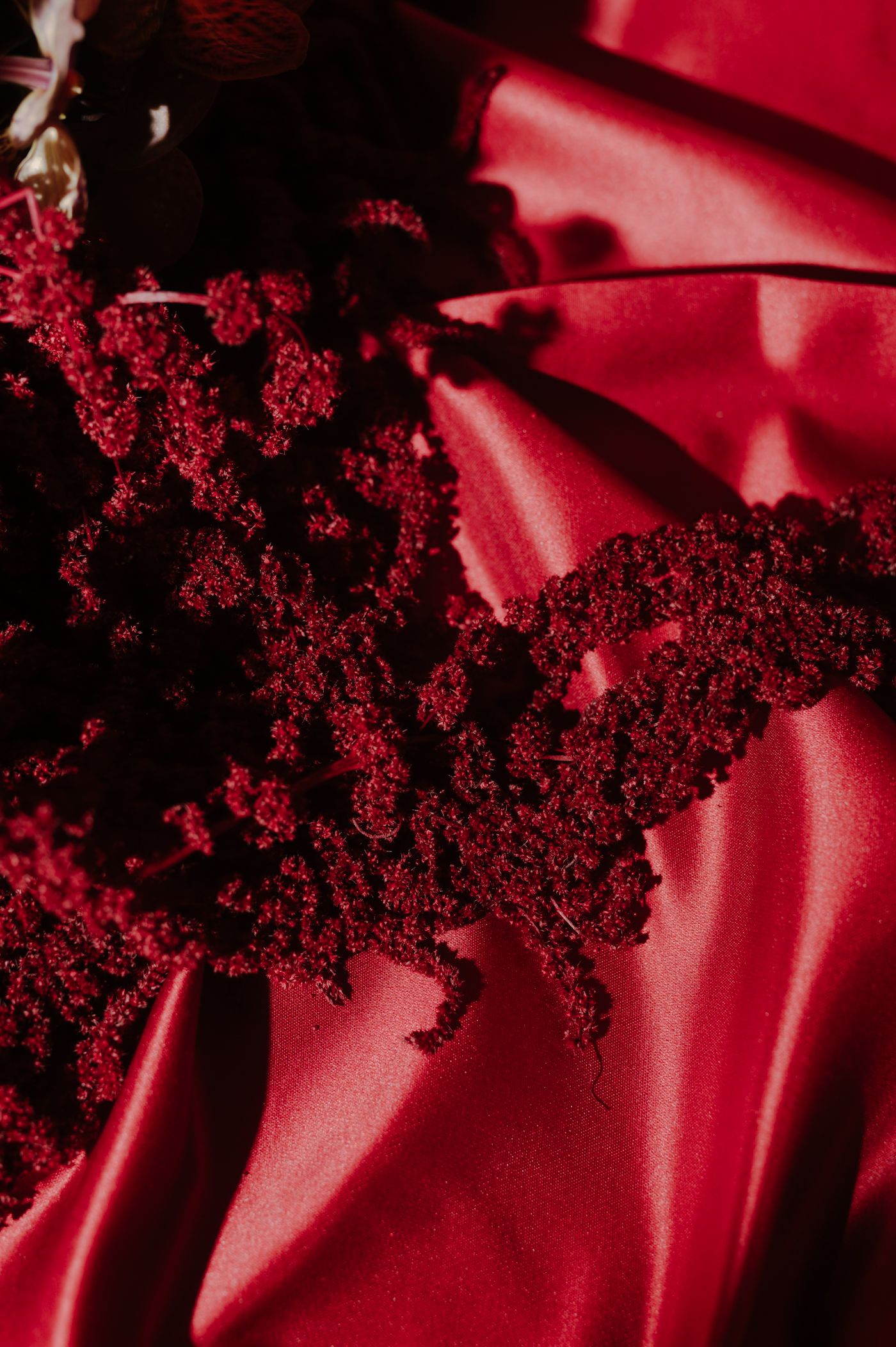 Close-up of deep red glitter or sparkly texture against a silky red fabric background creating a luxurious abstract pattern.