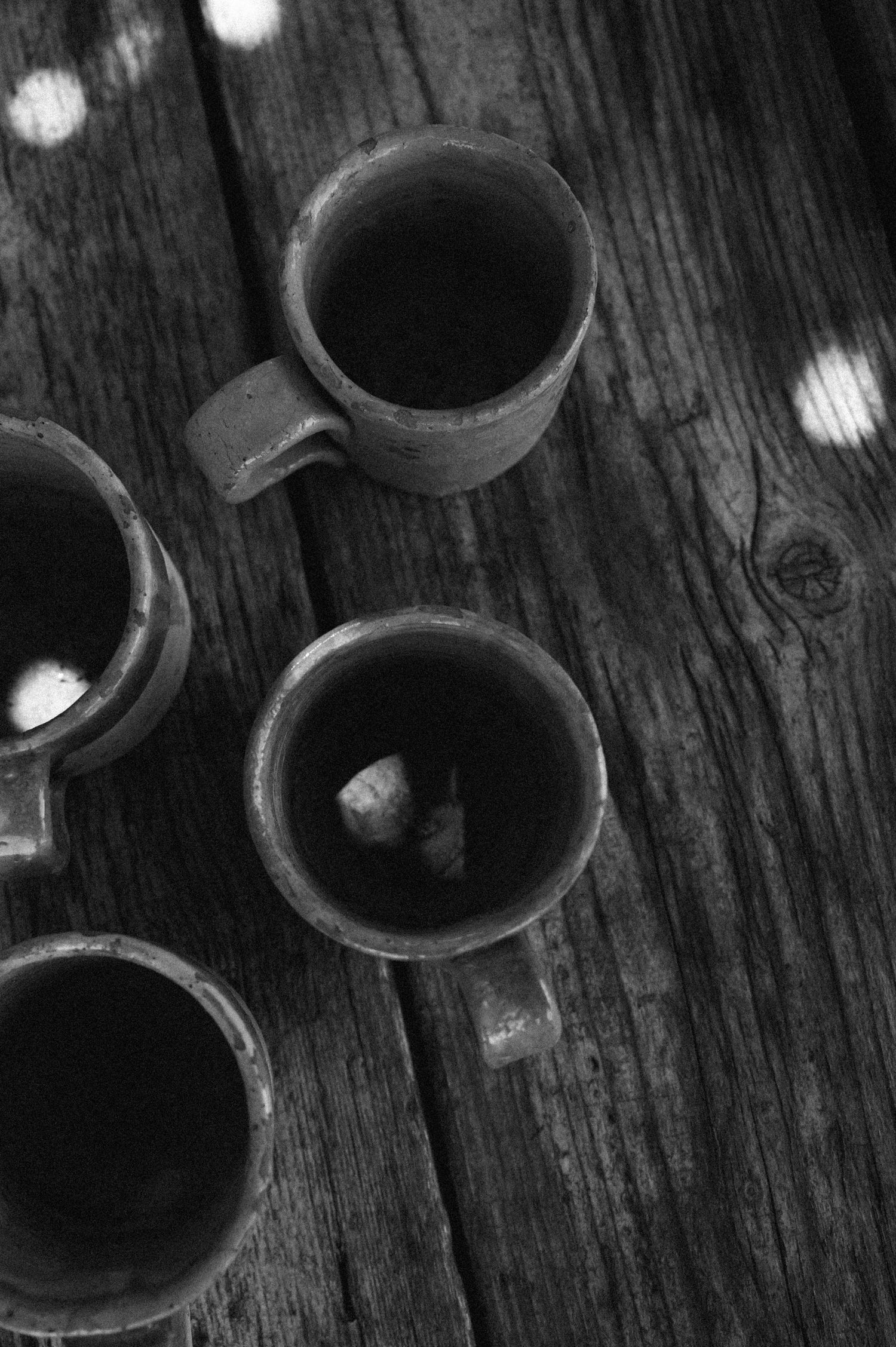 Black and white close-up of curved shapes casting shadows on weathered wooden surface with light spots.