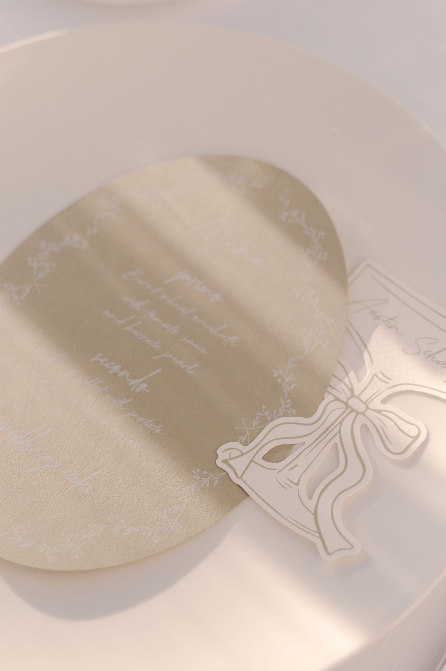 Elegant oval wedding menu card in soft gold on white plate with decorative bow place card.