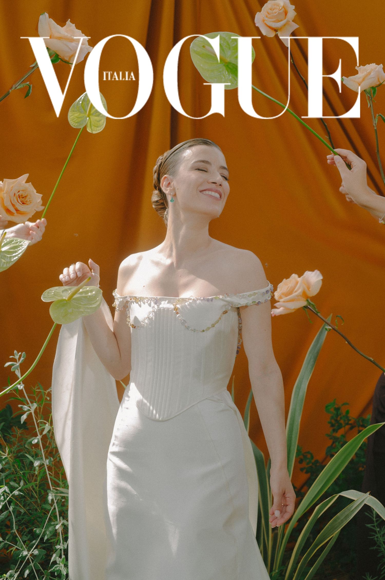 Fashion magazine cover showing a model in white dress against orange backdrop with floral elements and Vogue Italia branding.