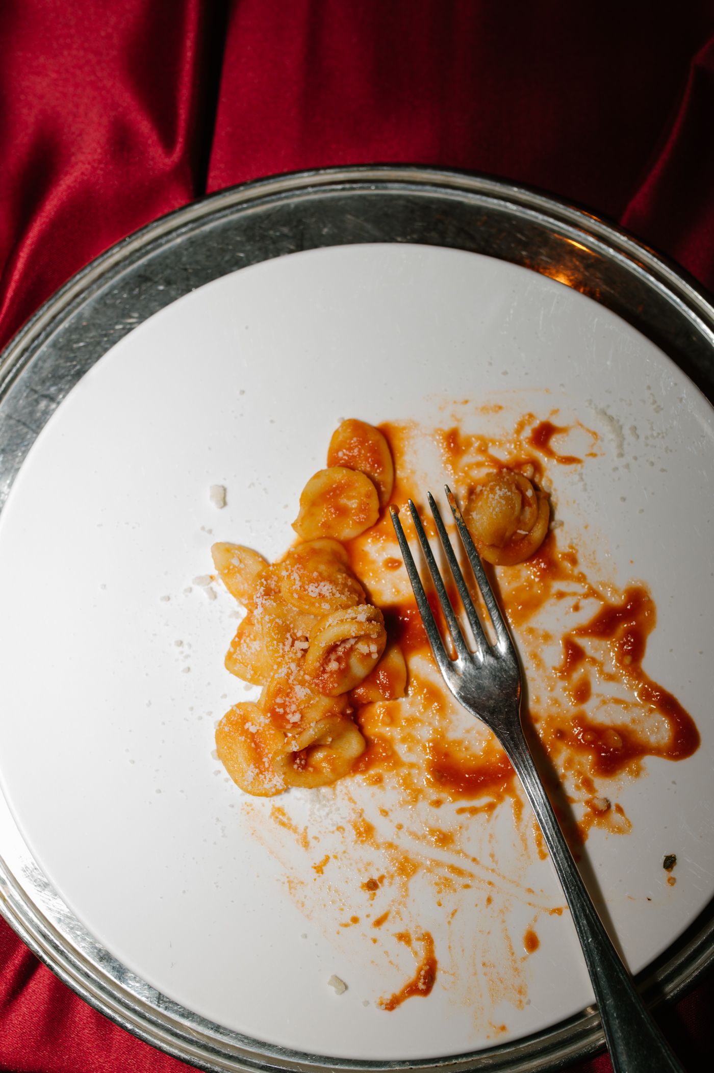 A nearly empty white plate with leftover orange sauce and a fork against a red cloth background.