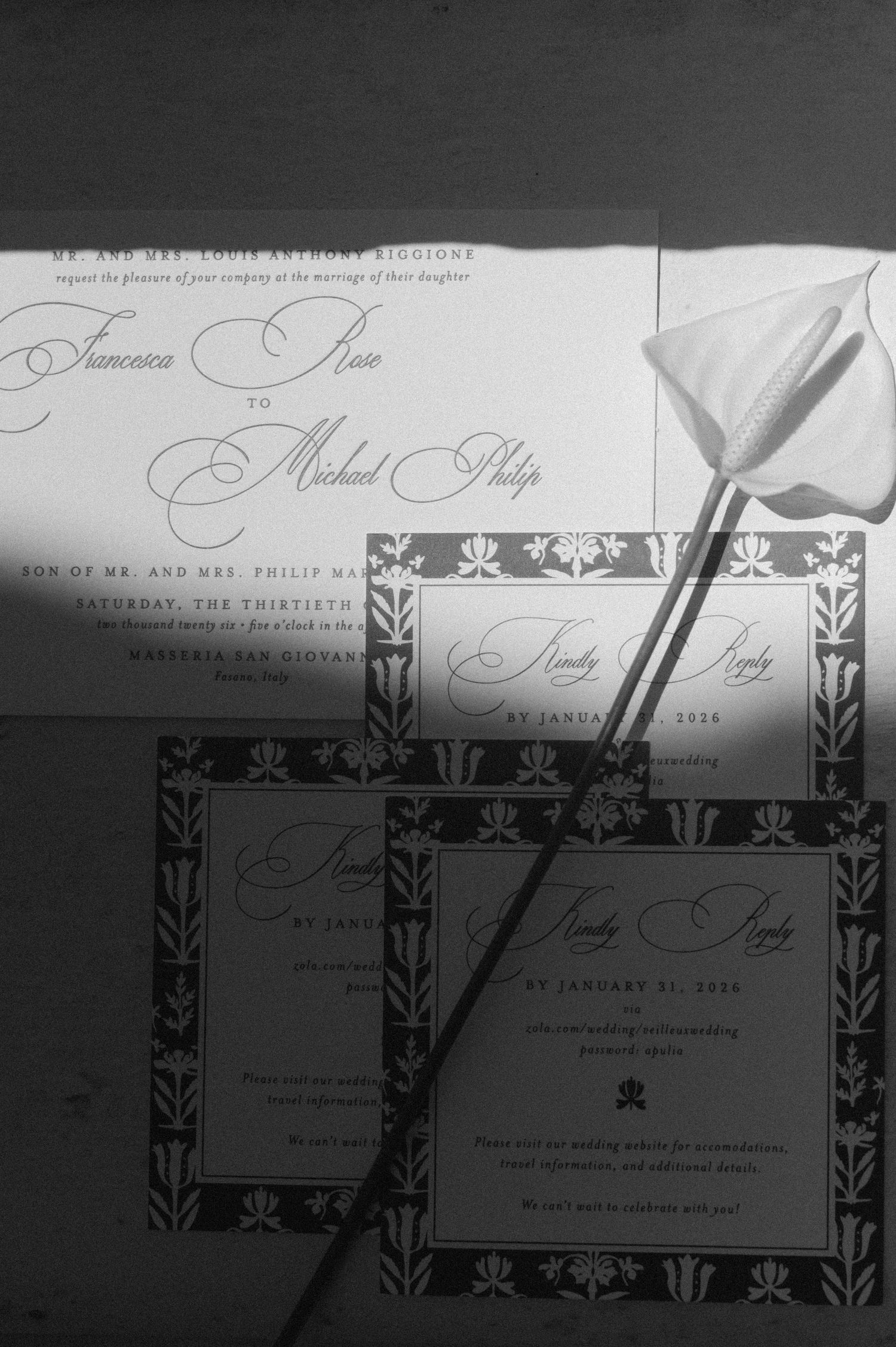 Black and white photo of elegant wedding invitations with floral border design and a single calla lily flower.