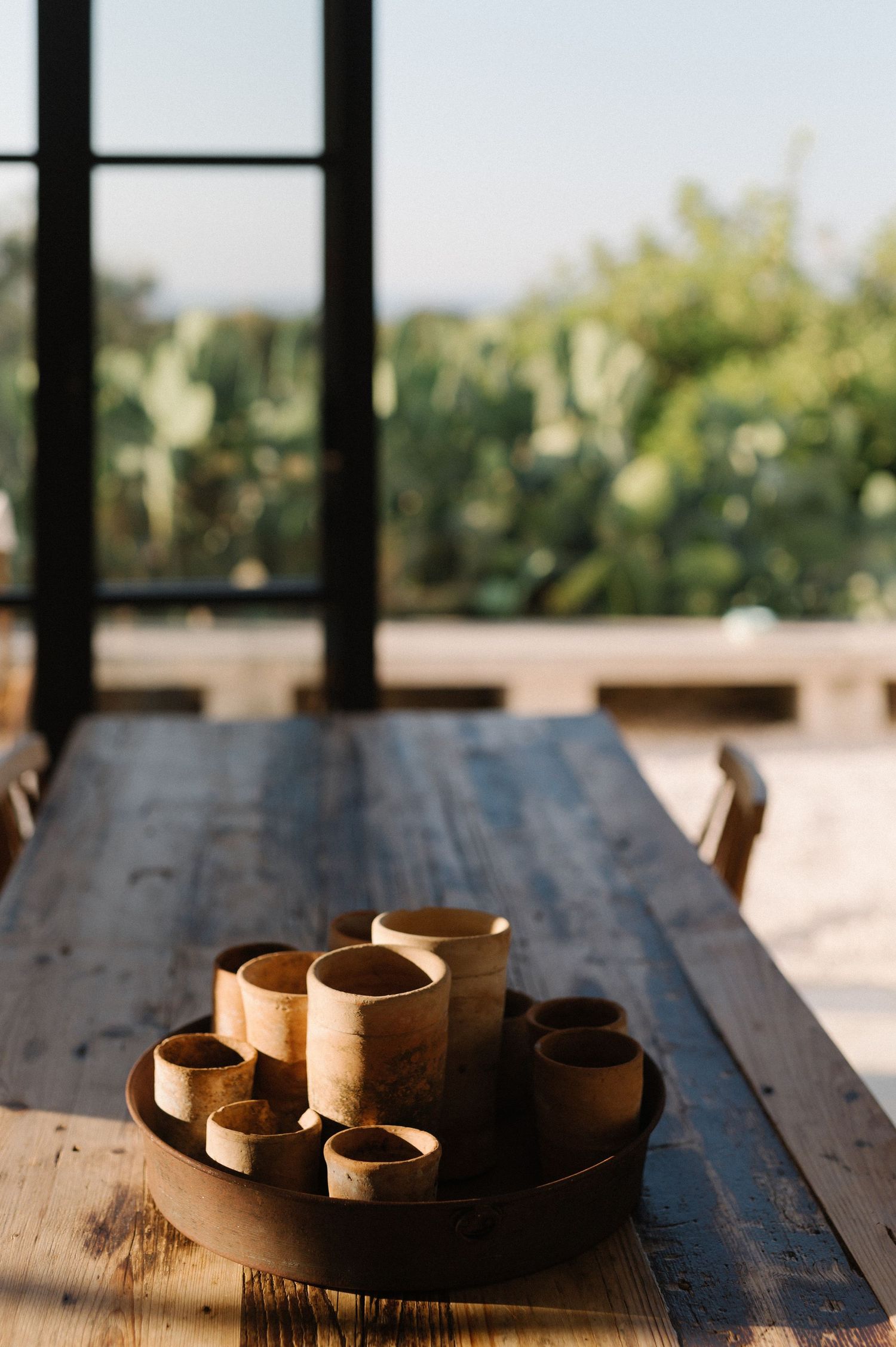 Rustic wooden table with handcrafted clay pots and ceramic vessels arranged in natural sunlight through window.