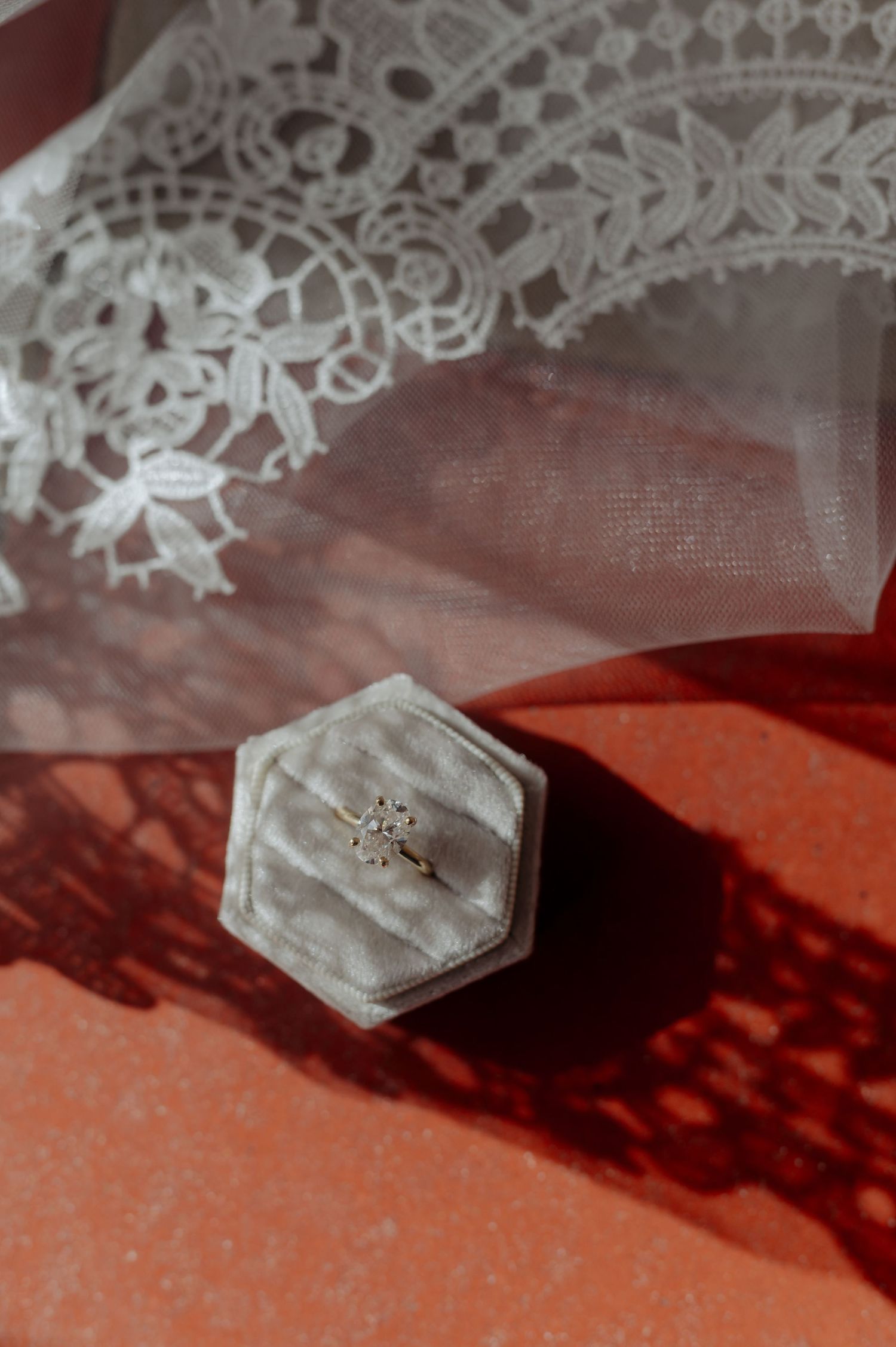 A delicate white lace doily with a small hexagonal jewelry box casting dramatic shadows on a rust-colored surface.