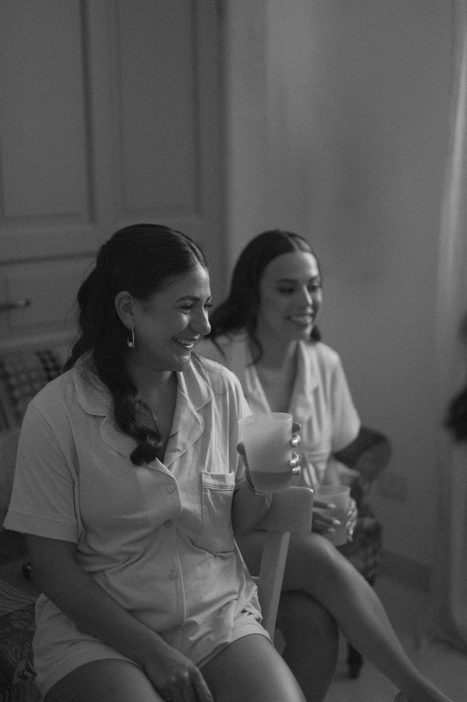 Two women in white pajamas laughing and holding mugs in a black and white photo.