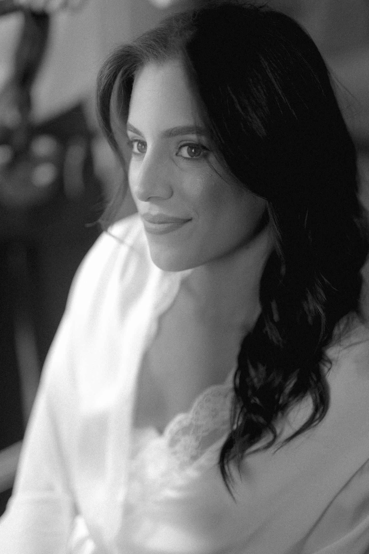 Black and white portrait of a beautiful dark-haired bride wearing a lace robe, smiling softly.