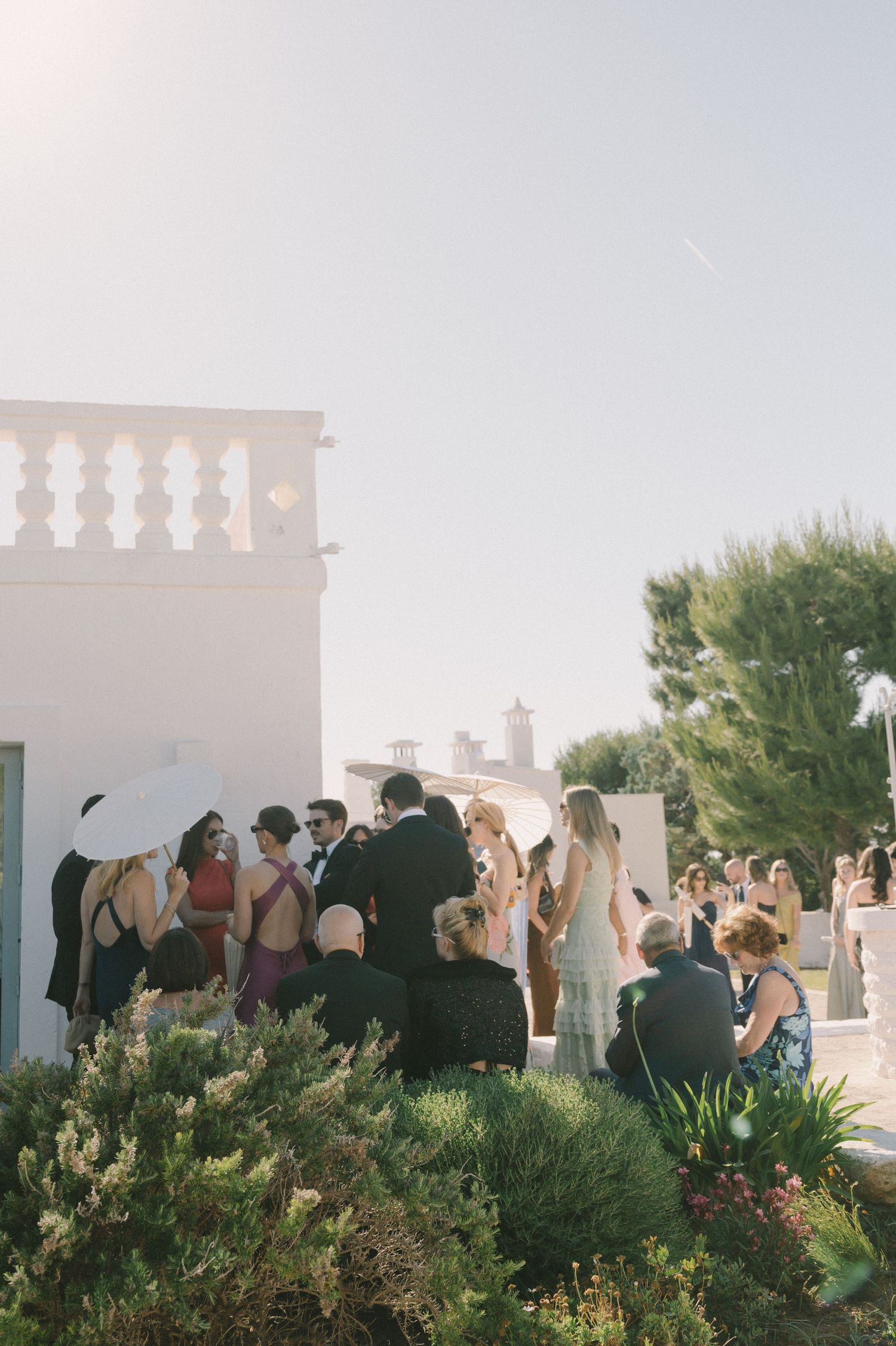 Outdoor wedding reception at a Mediterranean villa with elegantly dressed guests mingling in warm sunlight.