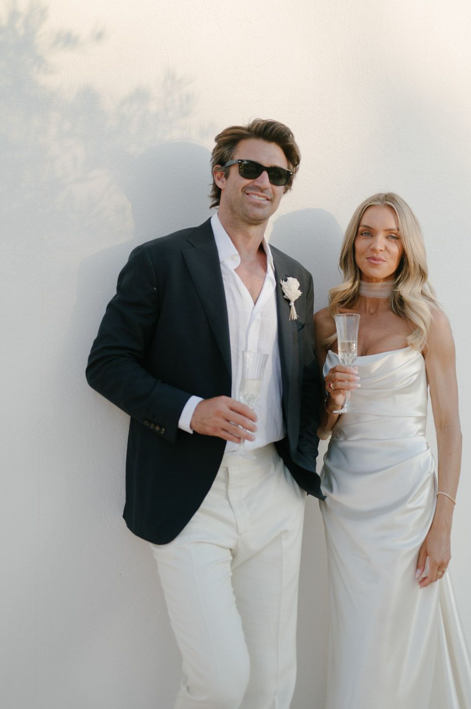 A couple in elegant white outfits poses together during a sunset celebration.