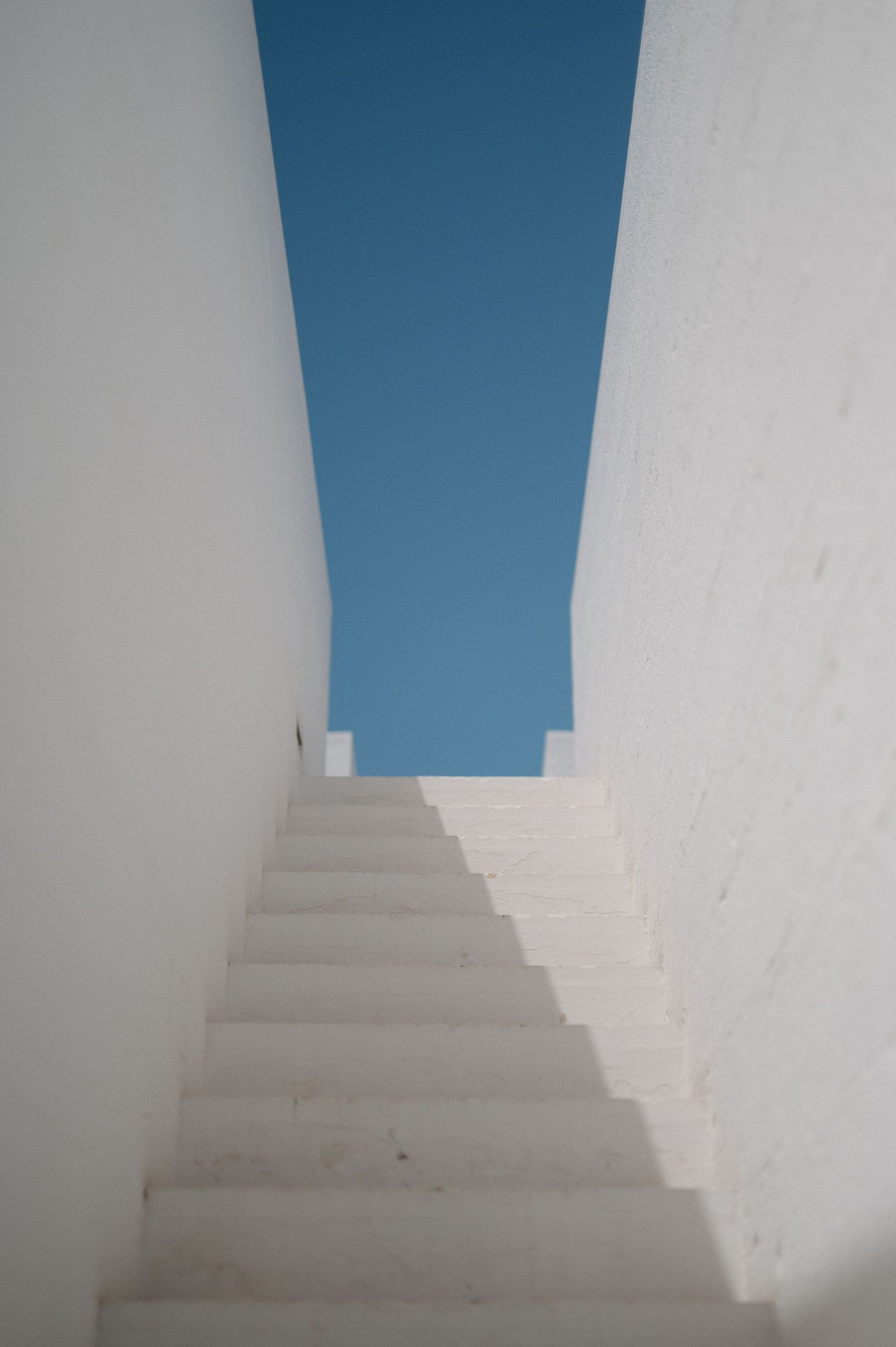 White staircase leading upwards with a bright blue sky visible through a narrow opening at the top.