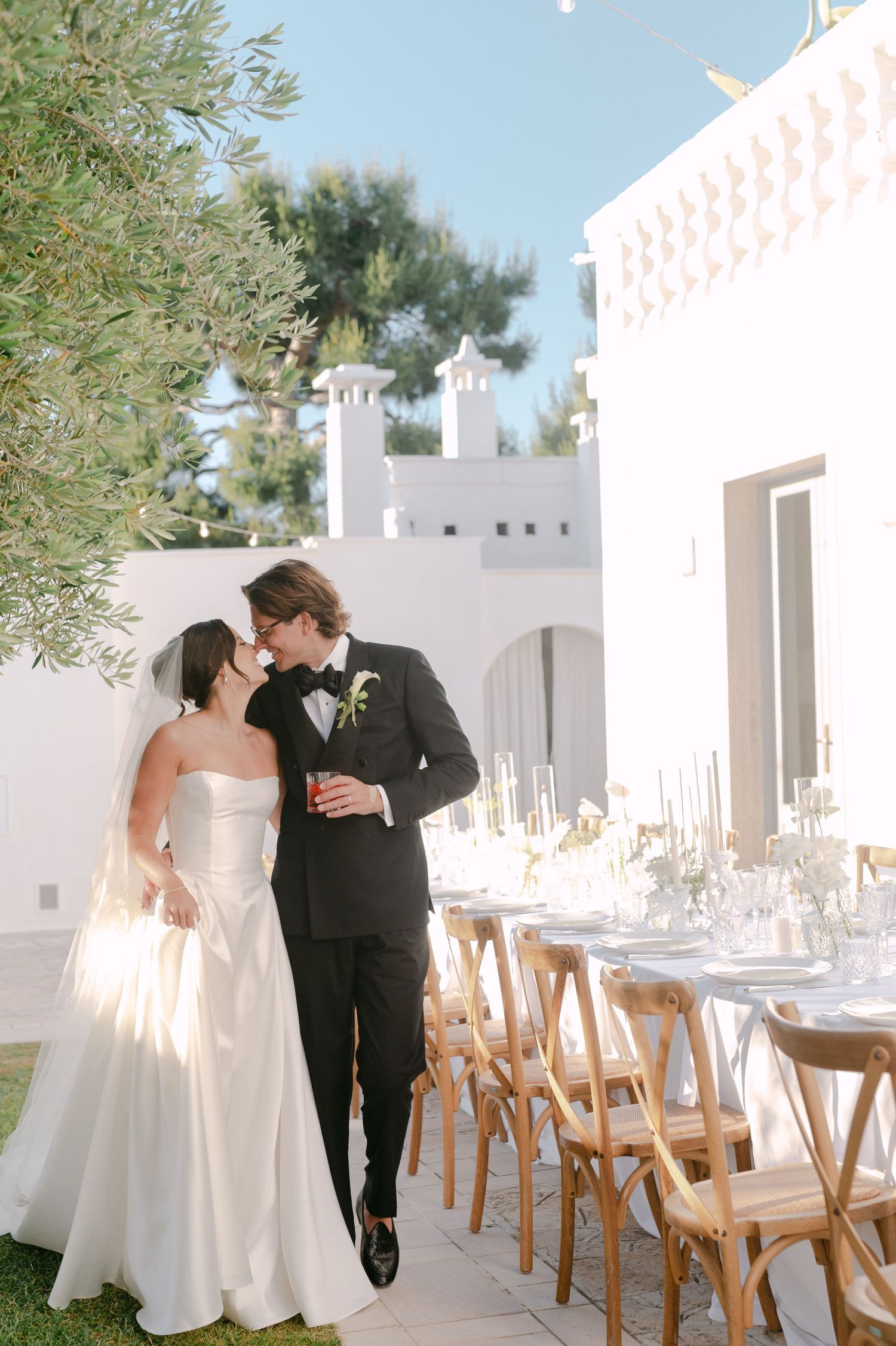 Bride and groom share a romantic moment outdoors at a white villa wedding venue with elegant long reception table.