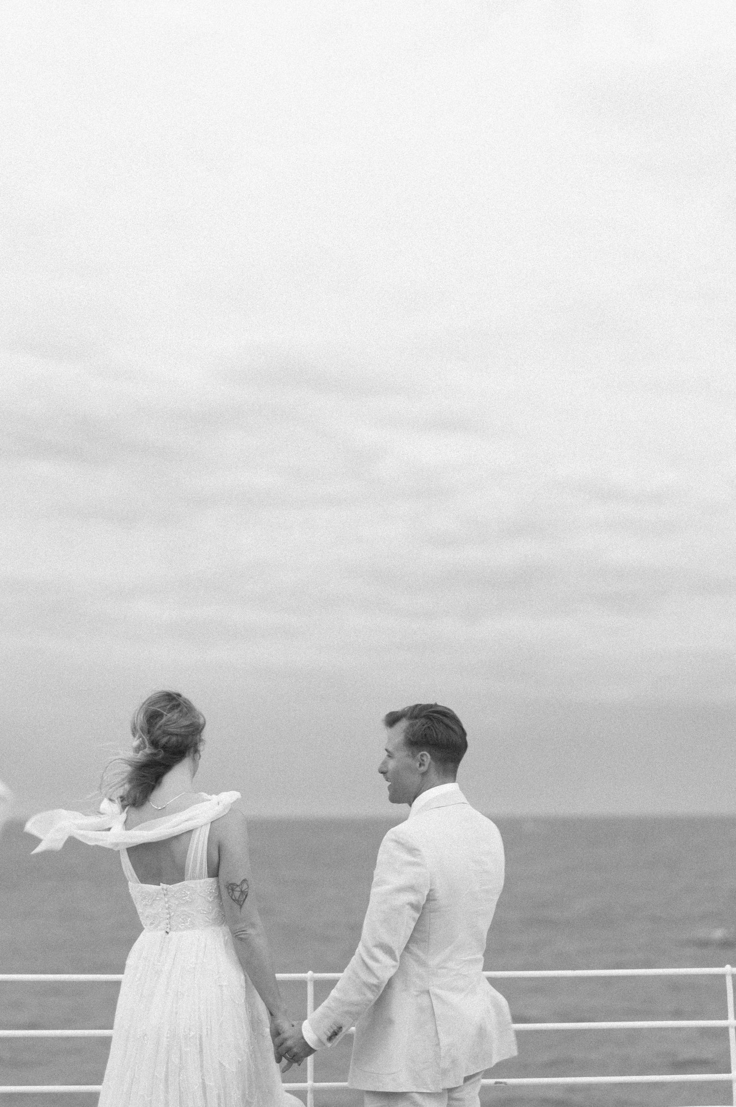 A couple in white attire sharing a romantic moment on a seaside balcony with ocean views.