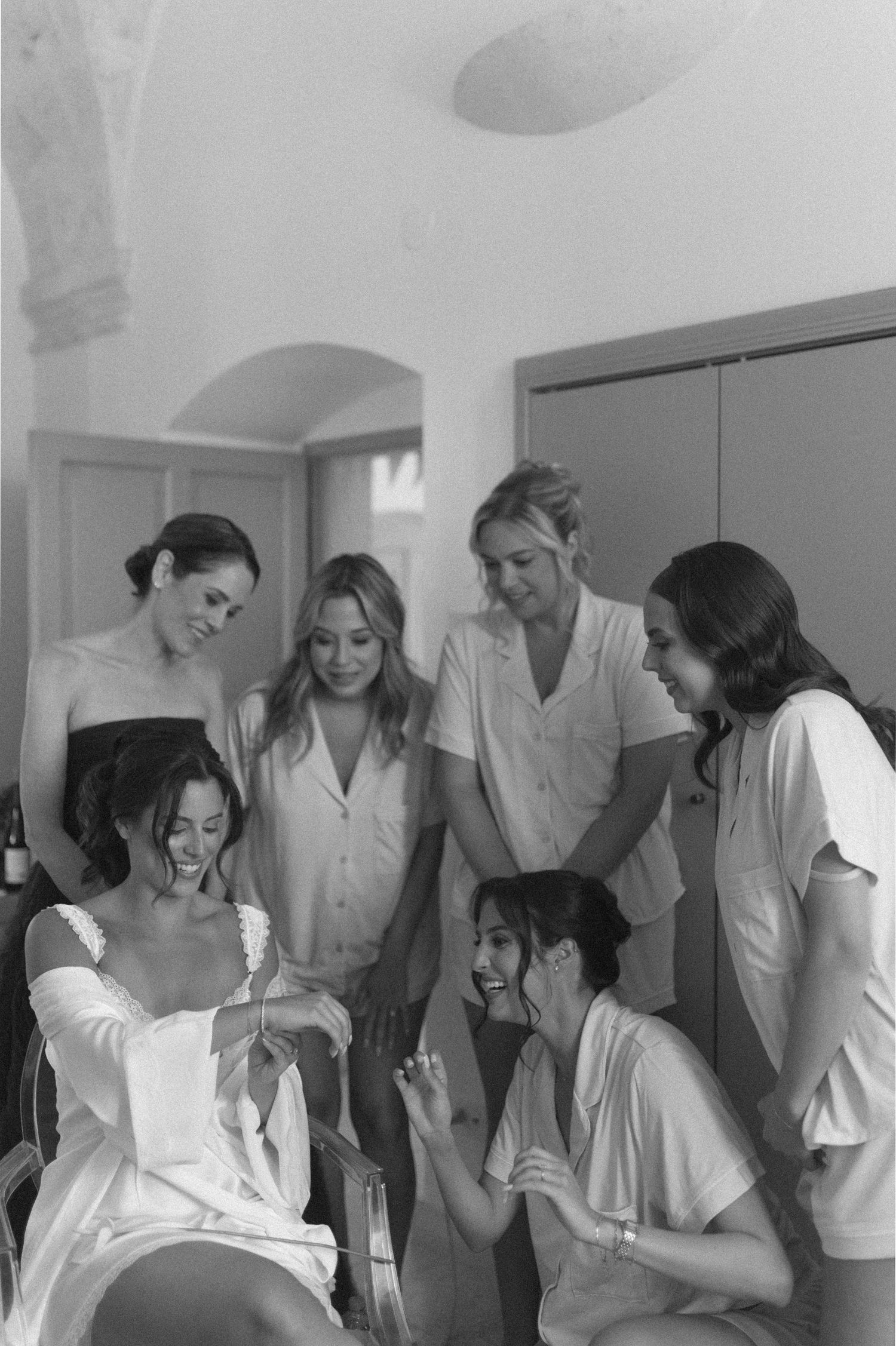 Bride laughing with bridesmaids in robes during wedding morning preparations, black and white photo.