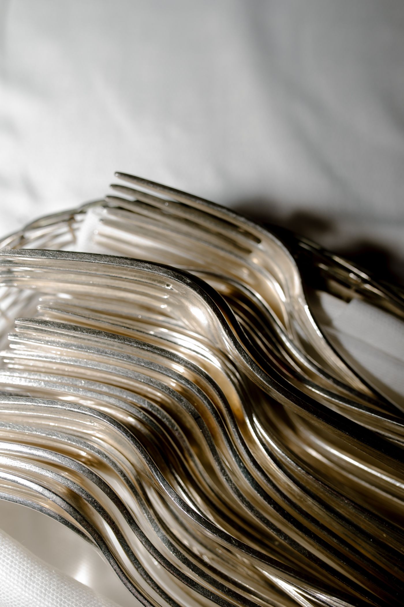 A close-up macro shot shows a neat stack of silver forks arranged in a wave-like pattern creating an abstract design.