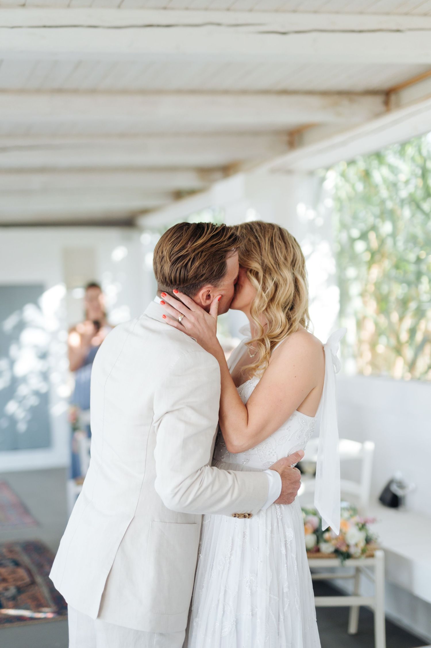 Romantic first kiss moment during wedding ceremony in a bright white room.