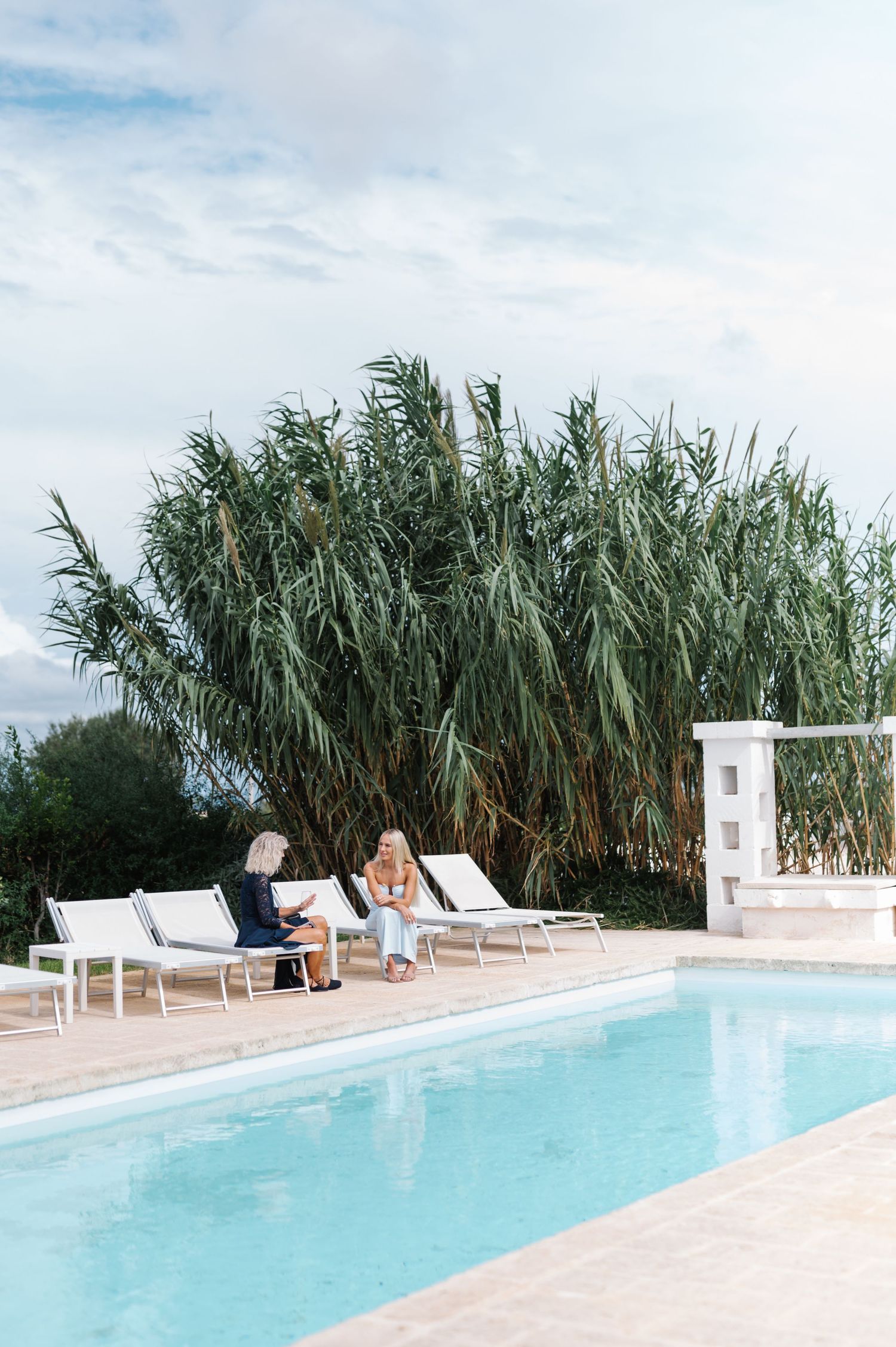 A serene swimming pool surrounded by tall reeds and white lounge chairs at a luxury resort.
