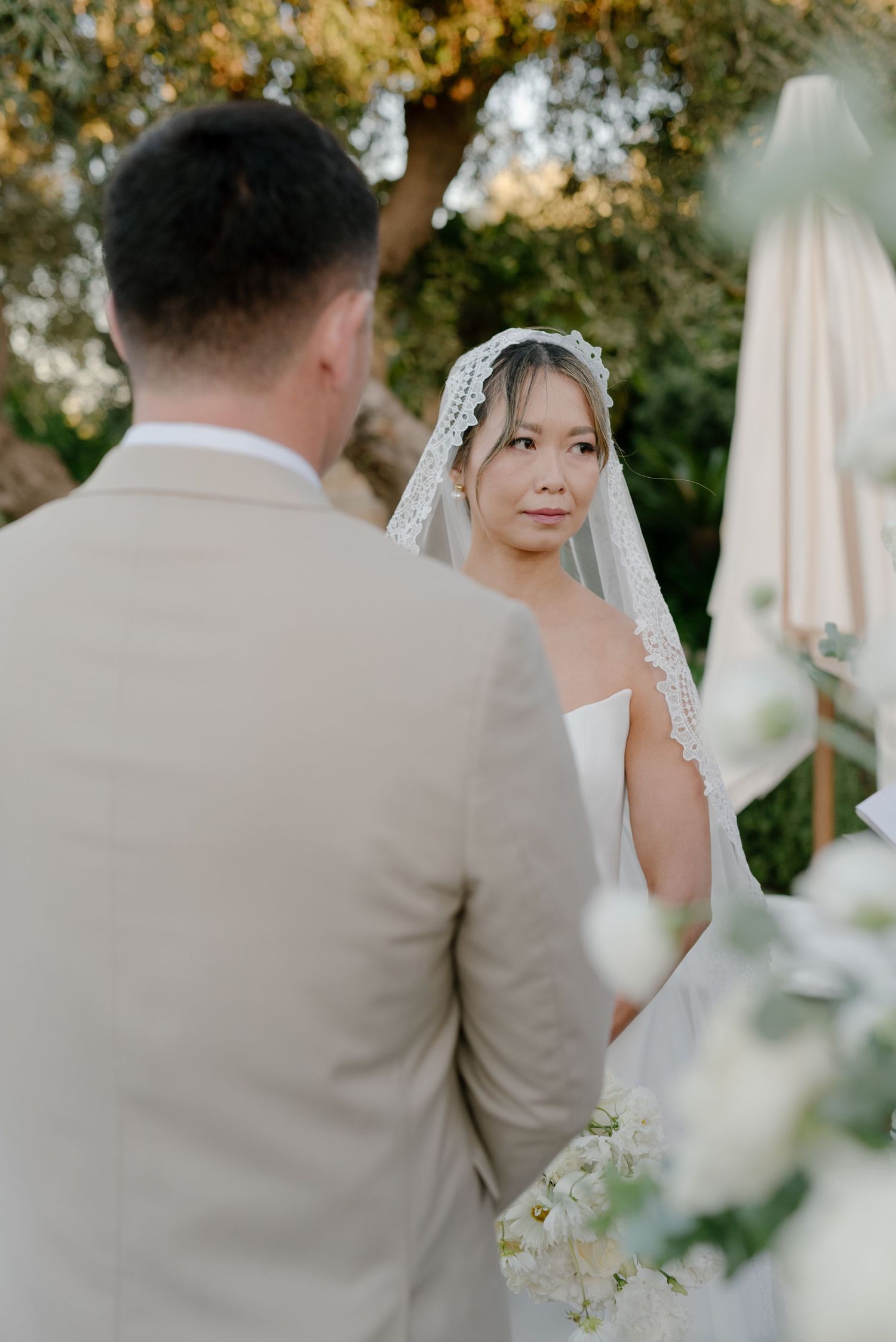 A bride and groom share an intimate moment during their outdoor wedding ceremony surrounded by white floral decor.