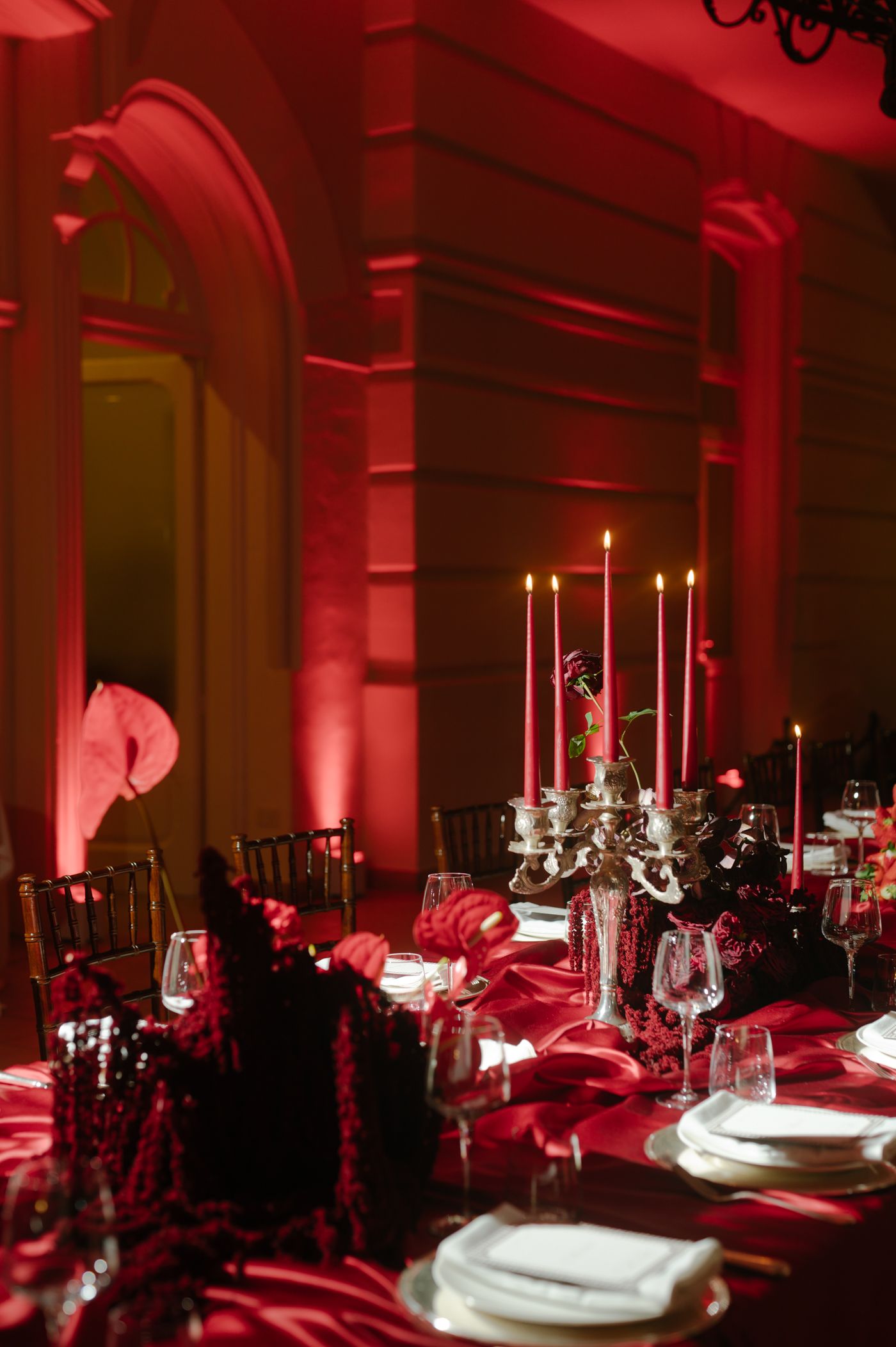 Elegant wedding reception tables set with black and red decor under dramatic red uplighting in a formal banquet hall.