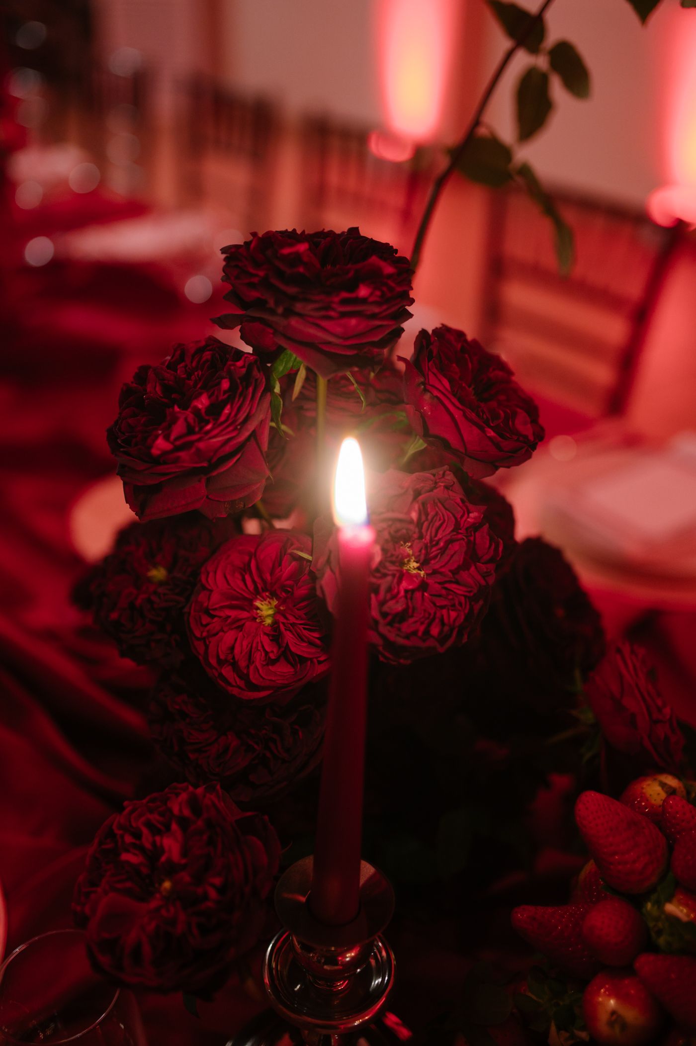 Deep red roses arranged in a vase glow under dramatic lighting creating a moody romantic atmosphere.