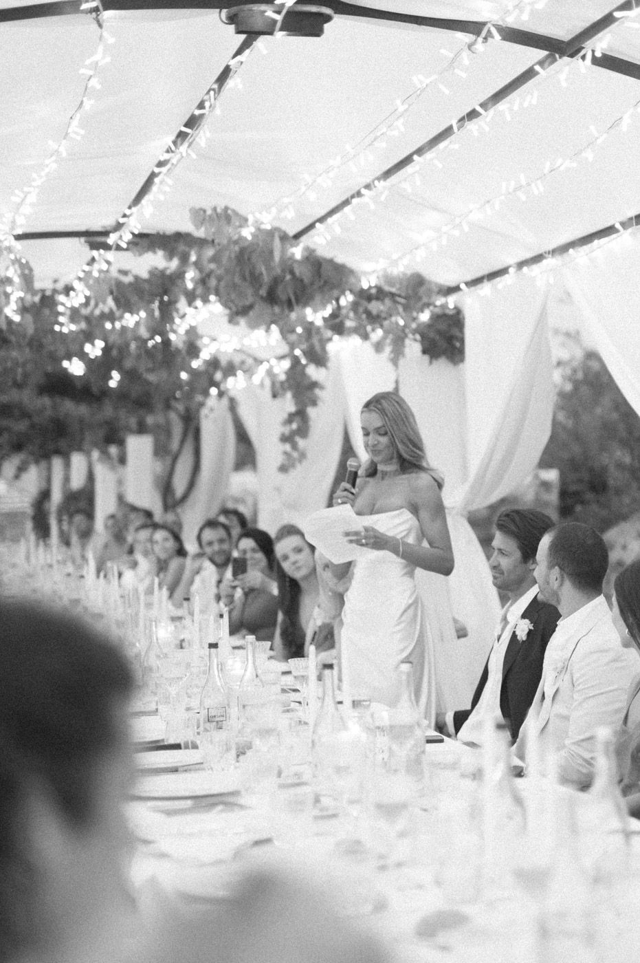 Wedding guests seated at long tables under string lights at an elegant outdoor reception.