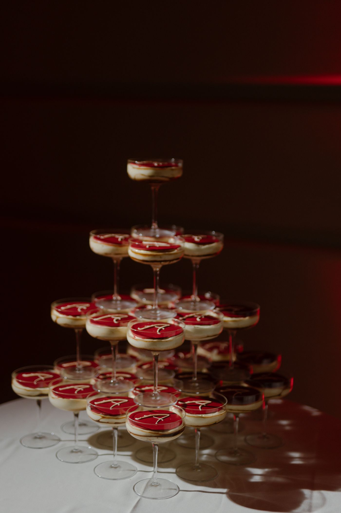 Multiple martini glasses filled with creamy desserts topped with red sauce arranged in a dark, moody setting.