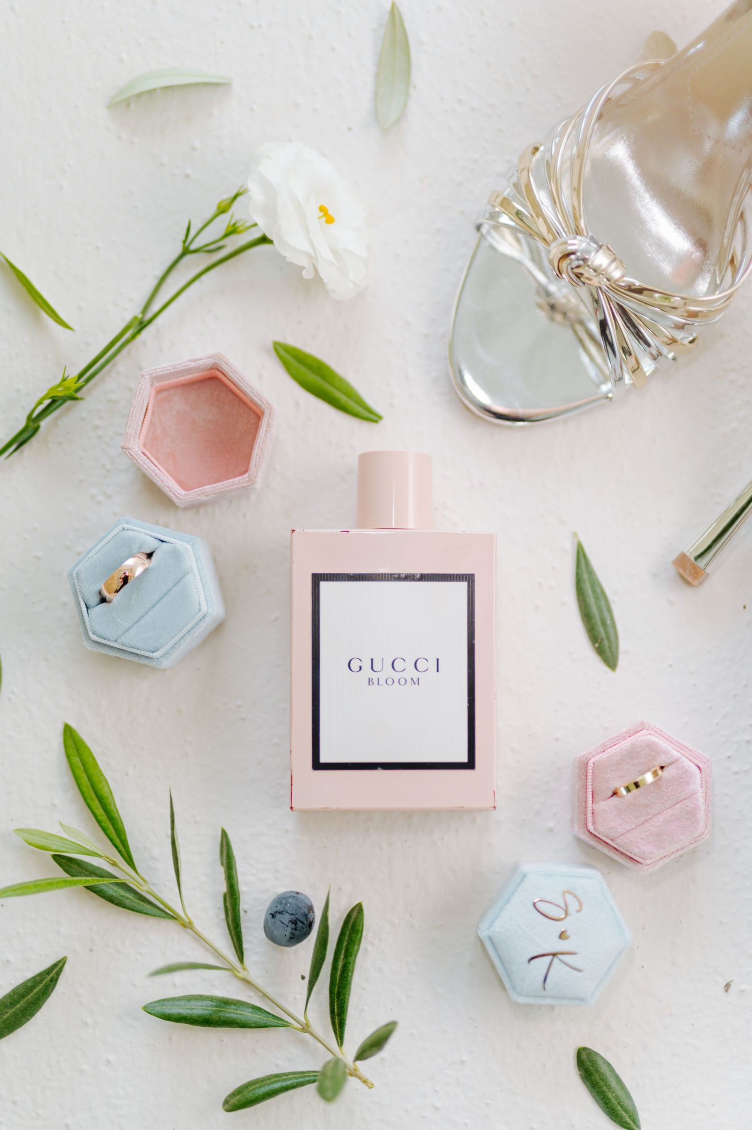 Delicate pink and blue hexagonal ring boxes with olive branches and Gucci perfume bottle on white surface.