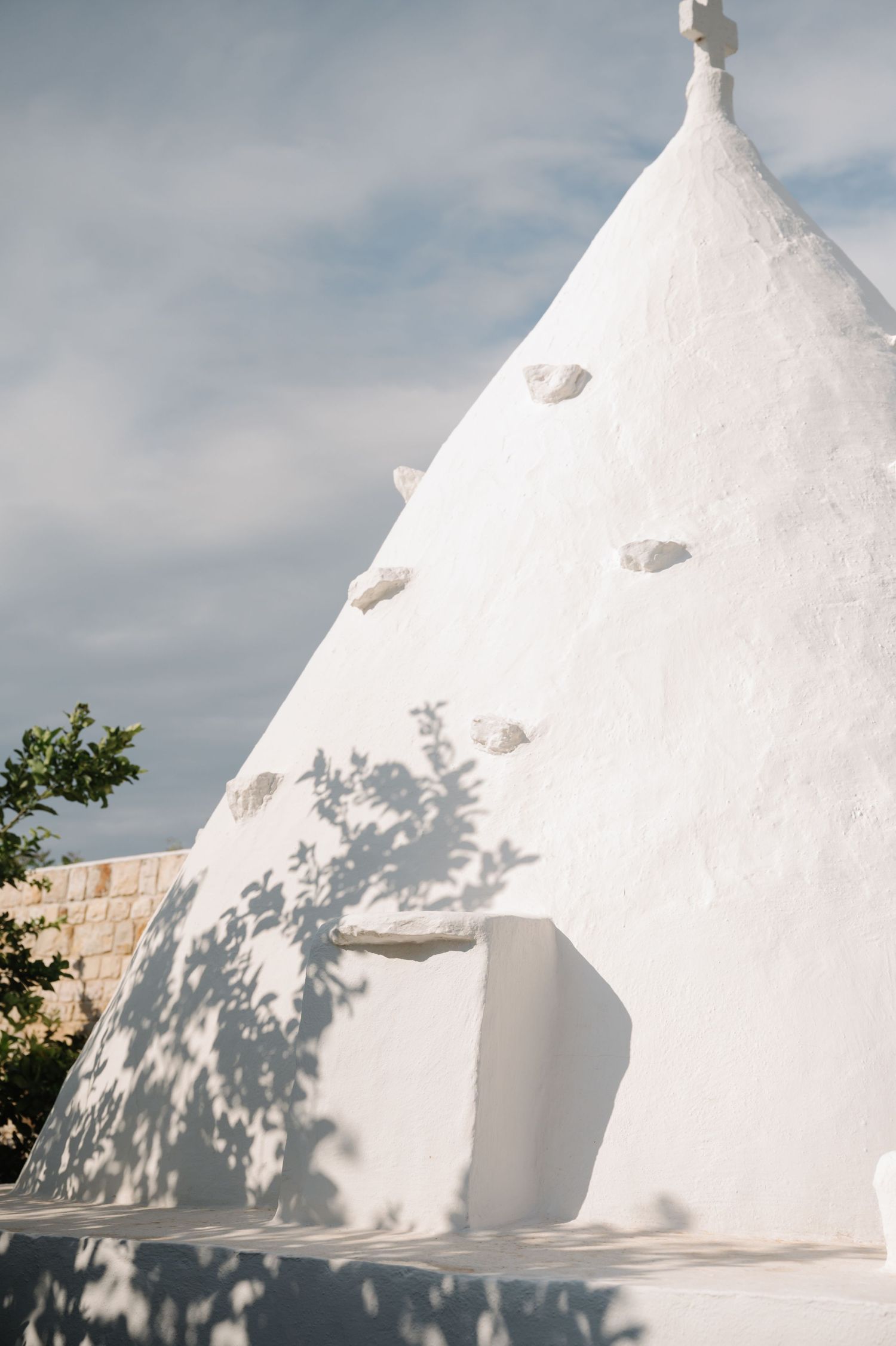 White conical trulli buildings casting shadows against bright sunlit walls.