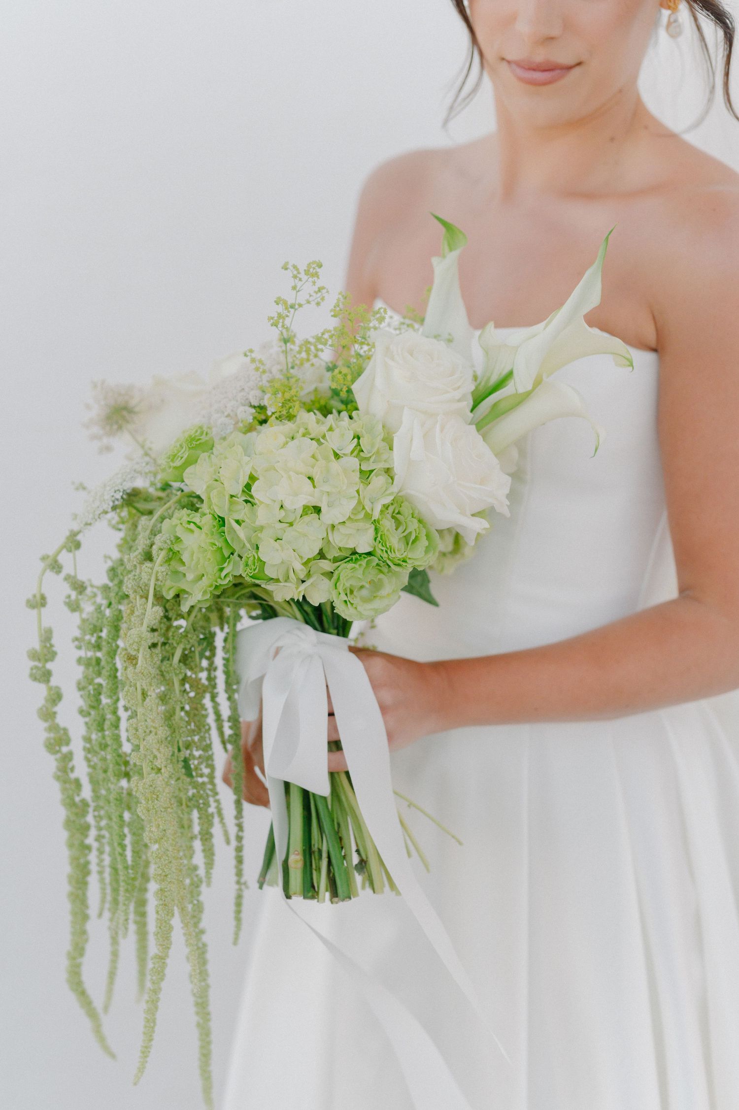 Bride in white strapless gown holding lush green and white wedding bouquet with cascading amaranthus and ribbon wrap.
