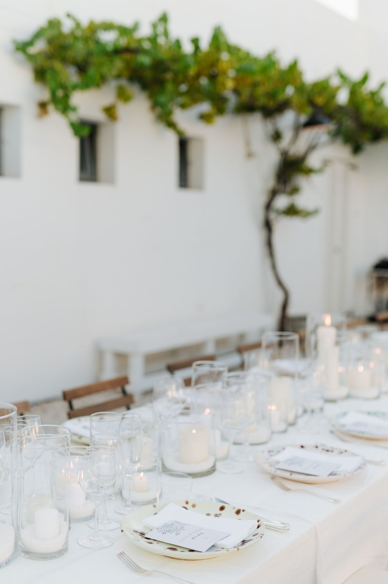 Elegant white dining table set with glowing candles and greenery decor along the wall for an intimate gathering.