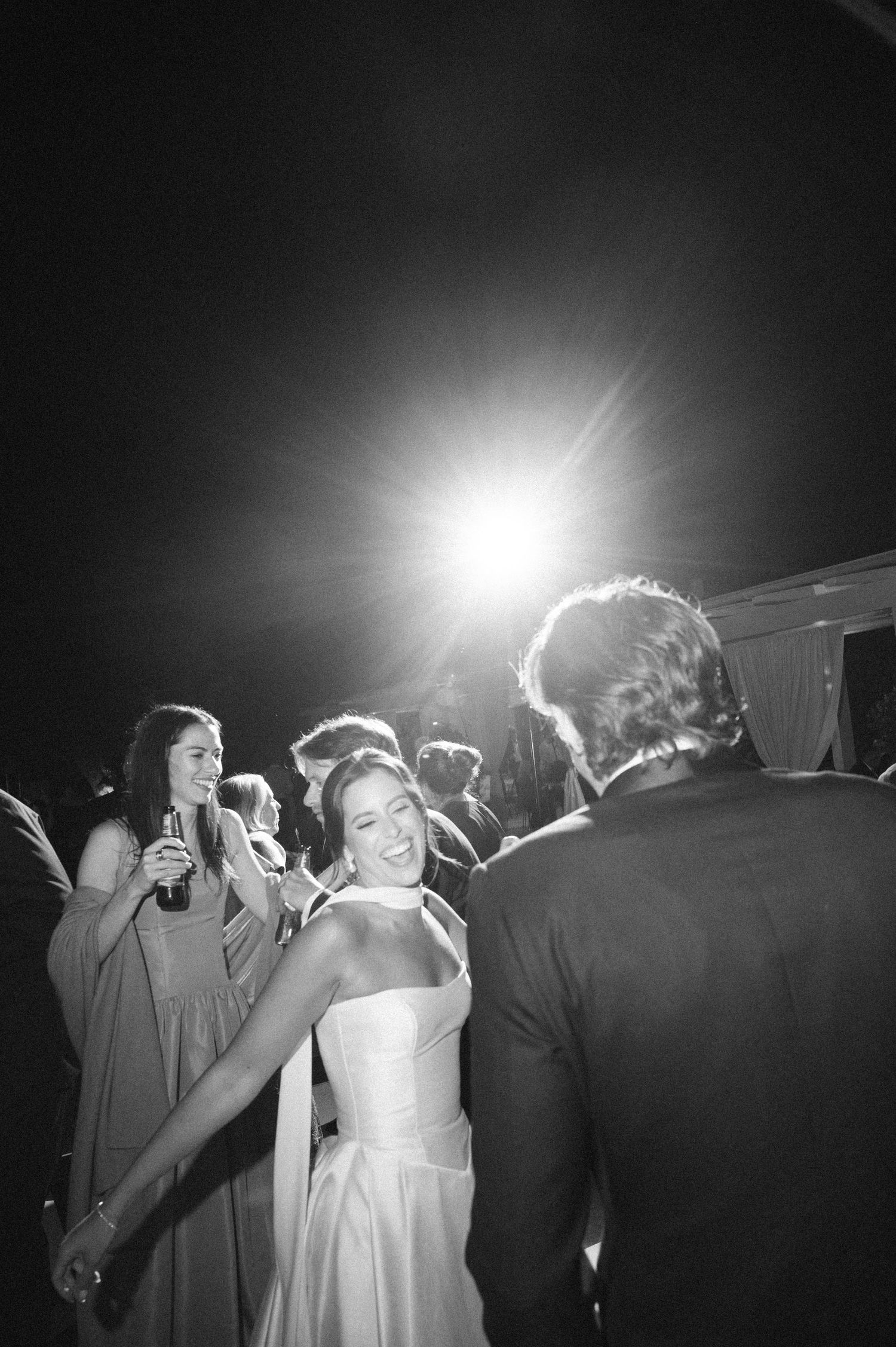 Black and white photo of a bride smiling while dancing with groom at a wedding reception.