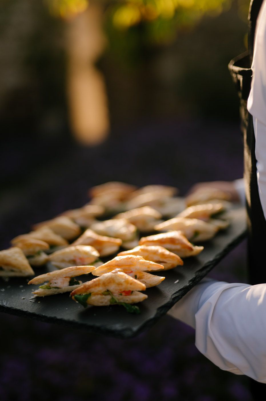 Appetizers arranged on dark slate serving platters at an elegant event.