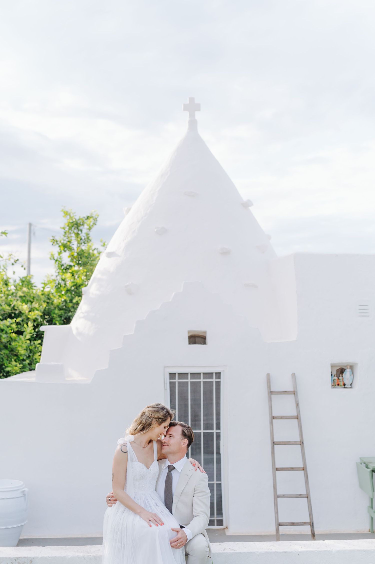 Wedding couple embracing near white Mediterranean buildings with wooden ladders.