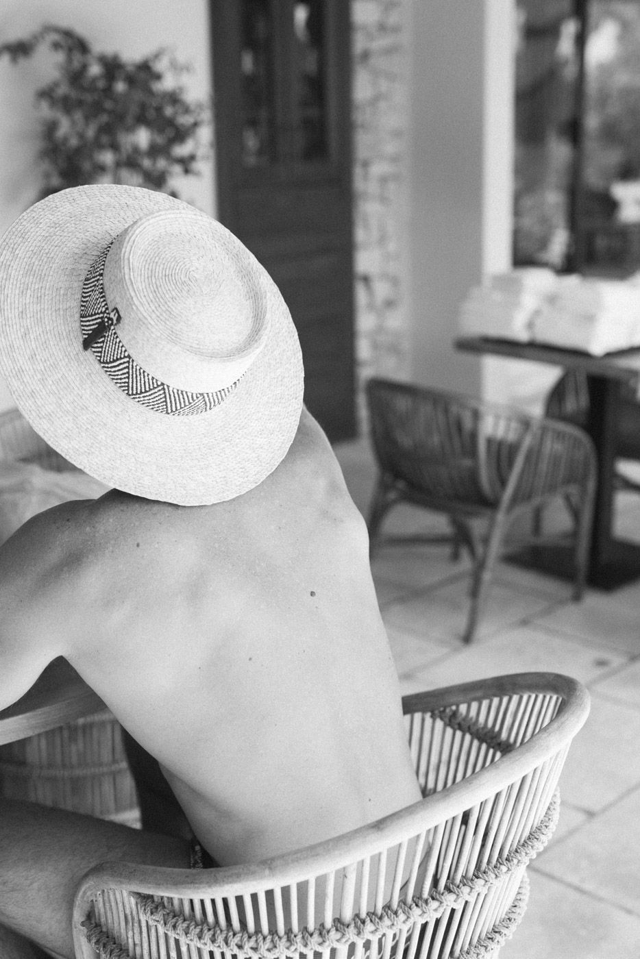 Person relaxing in a wicker chair wearing a white sunhat in black and white photography.