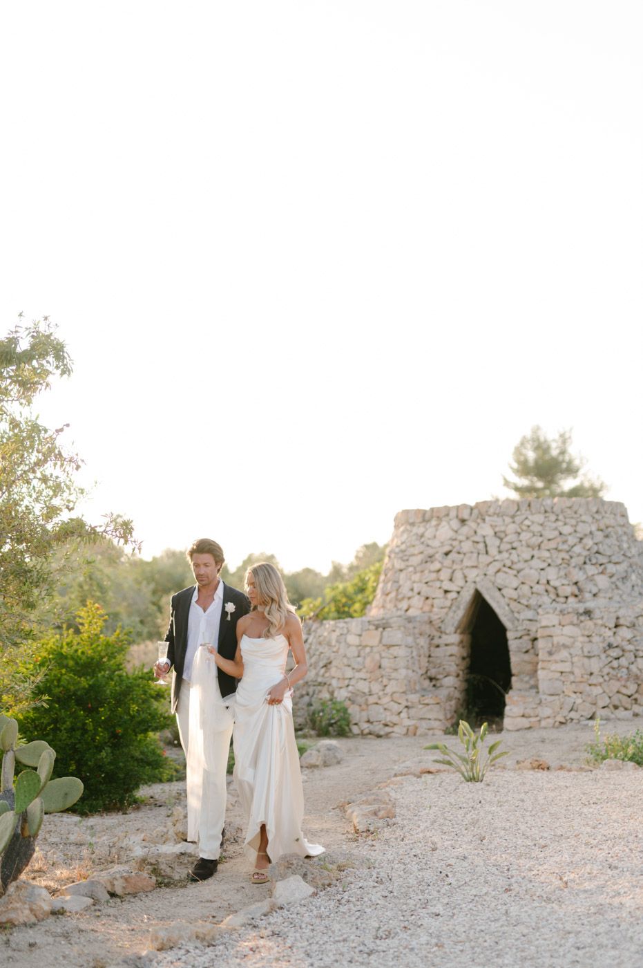 A couple in wedding attire explores a rustic stone landscape at sunset.