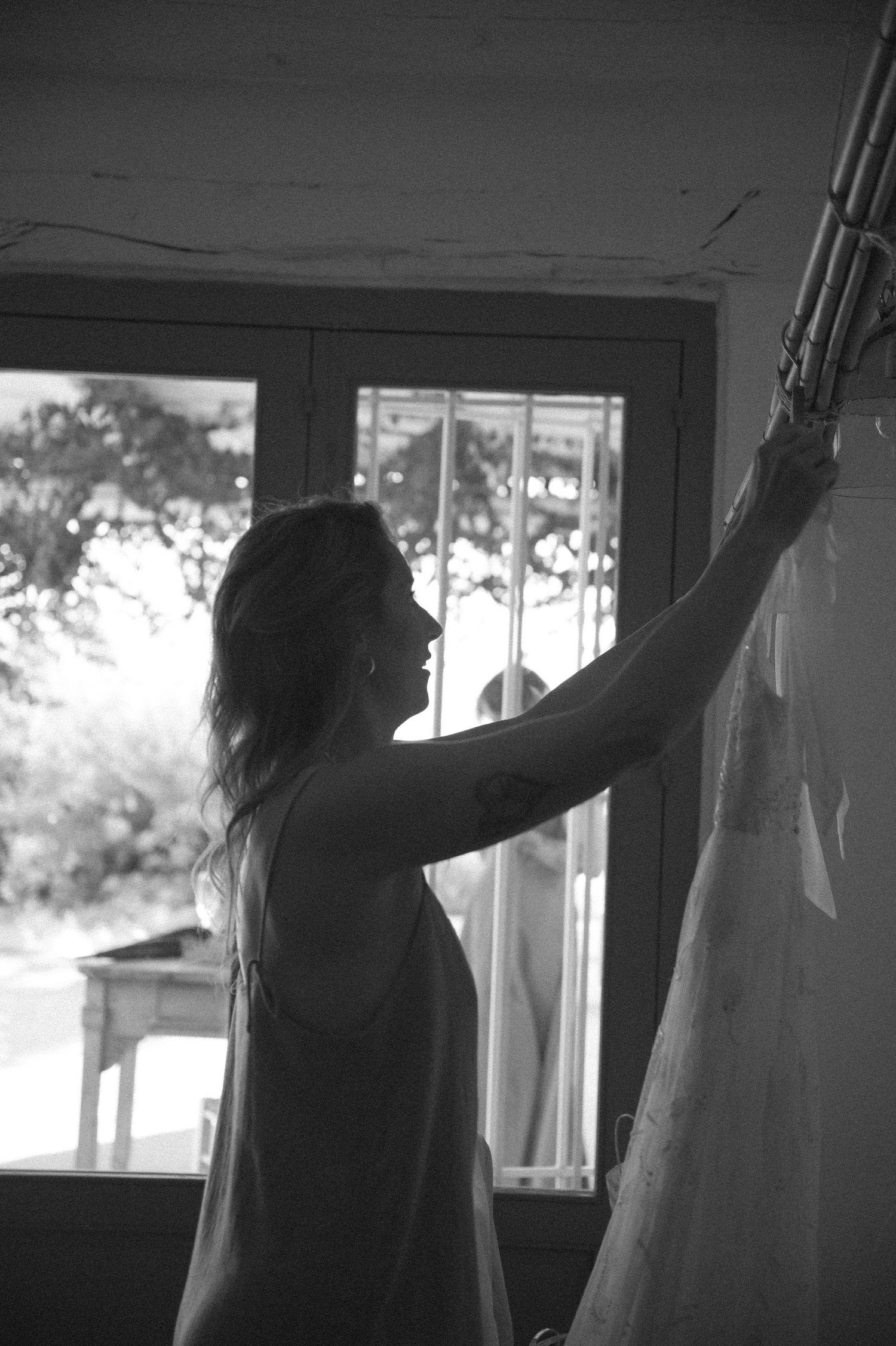 Silhouette hanging white fabric in front of sunlit windows.