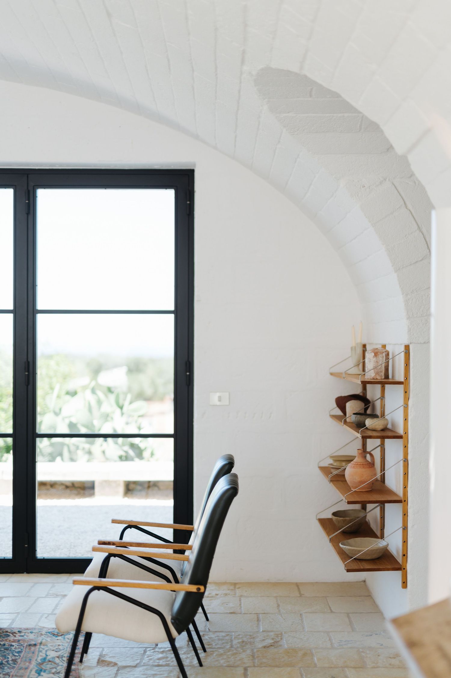 Modern interior with curved white walls, black-framed windows, and mid-century armchair against minimalist architecture.