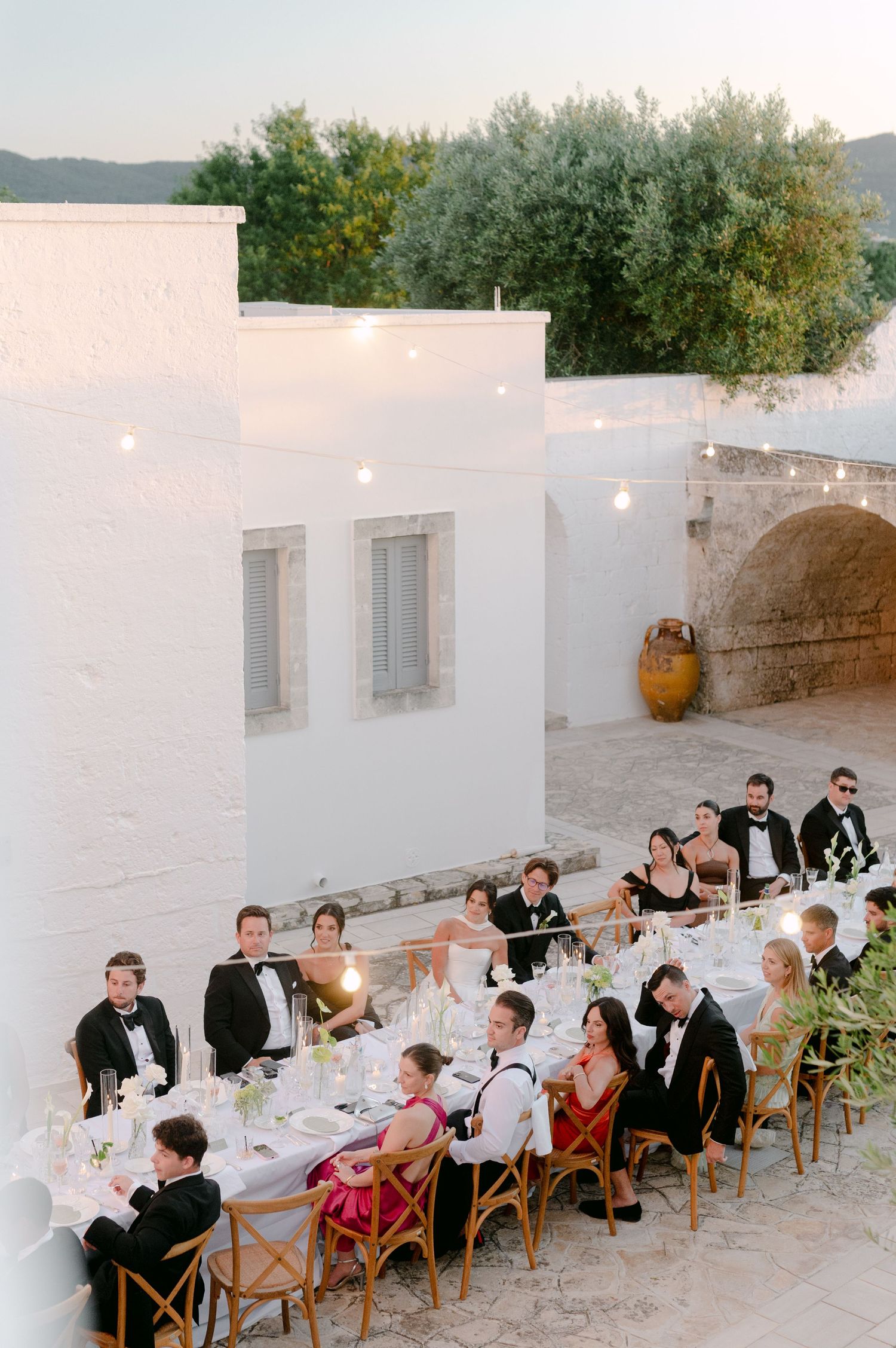 Elegant outdoor wedding reception at a white Mediterranean villa with string lights and long dining table at dusk.