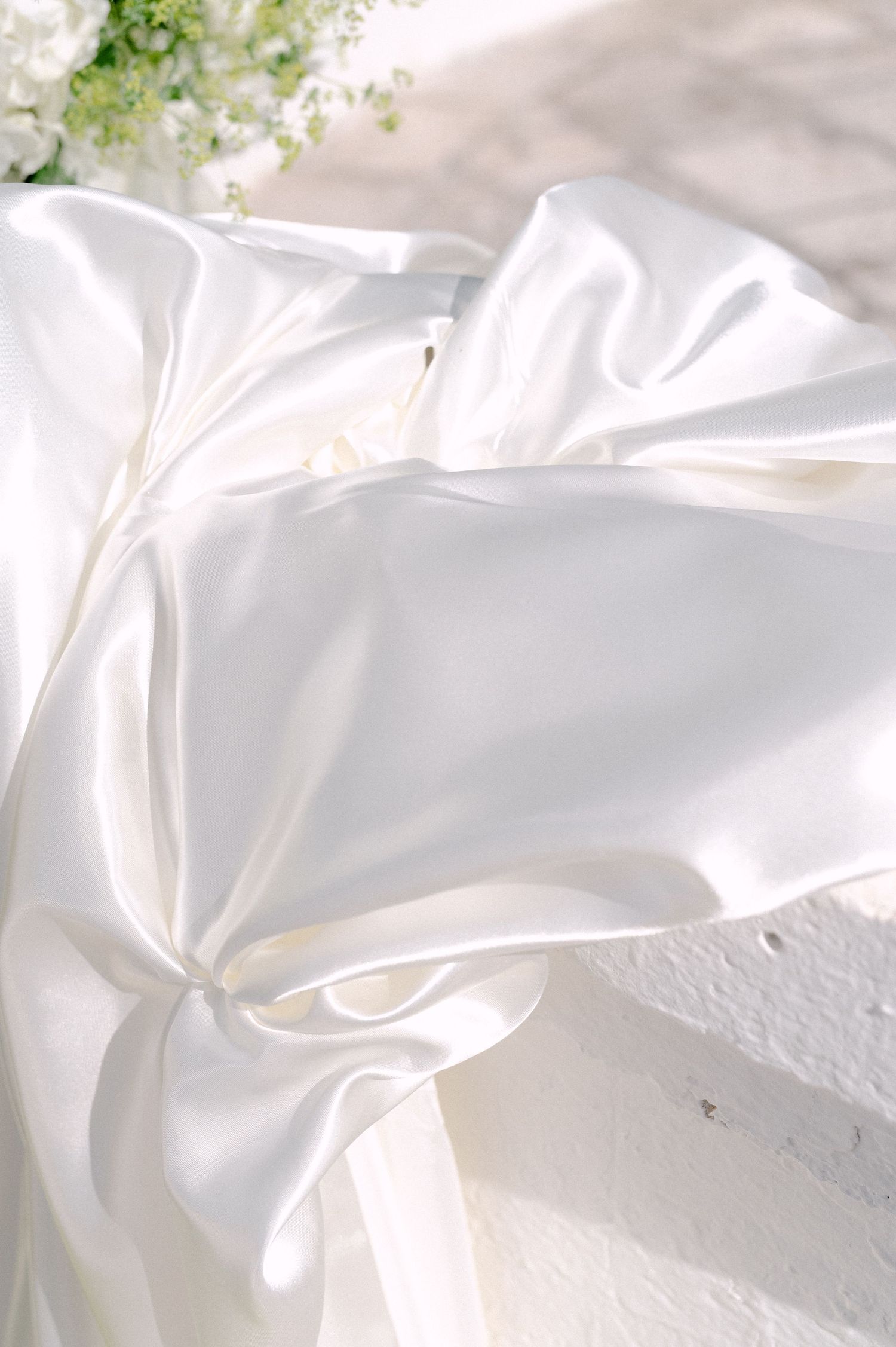 Elegant white satin fabric draped softly with white flowers in the background, perfect for luxury wedding decor.