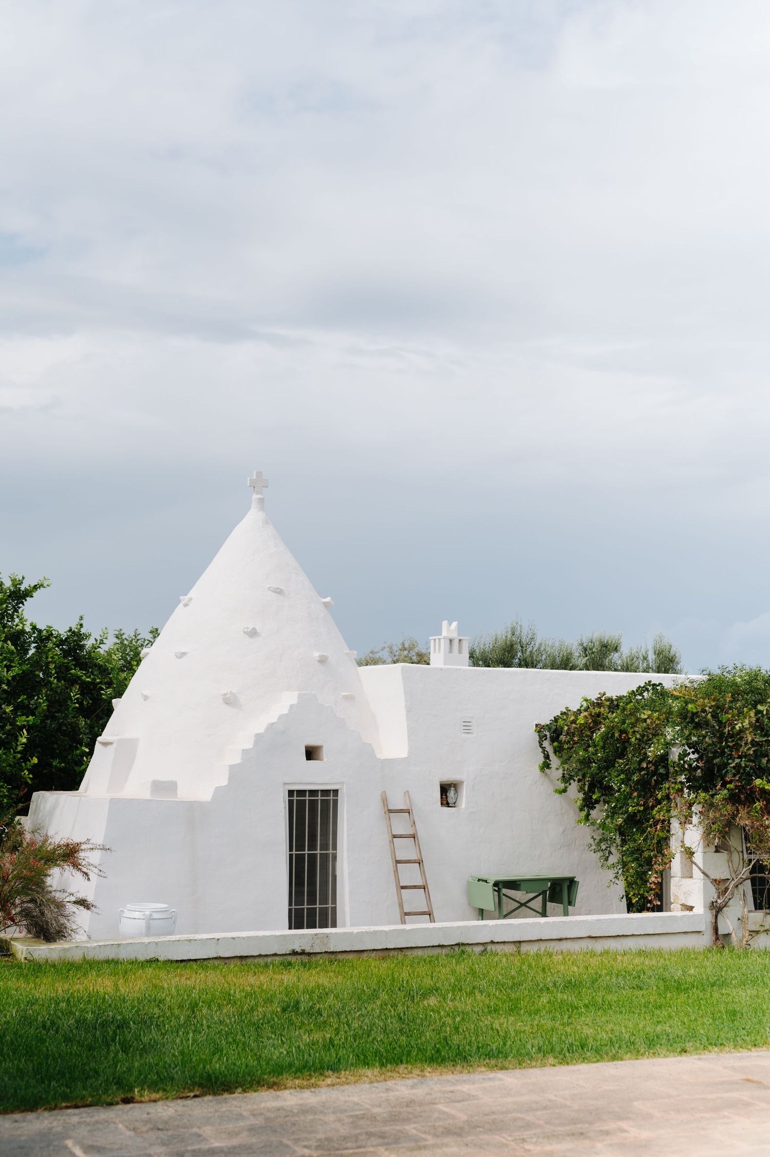Traditional white trulli buildings with conical roofs against cloudy sky in Puglia, Italy.