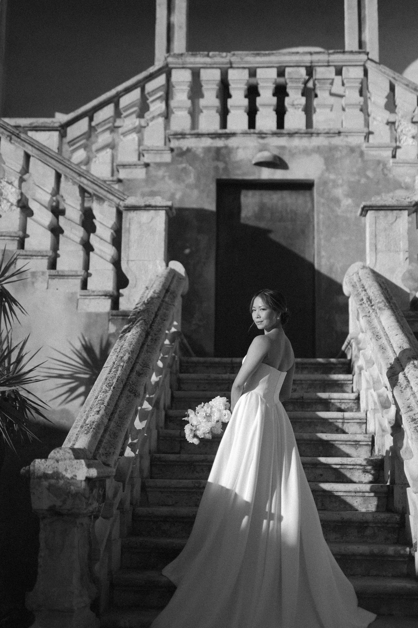 A series of black and white photos showing a couple in formal attire posing on an elegant stone staircase.