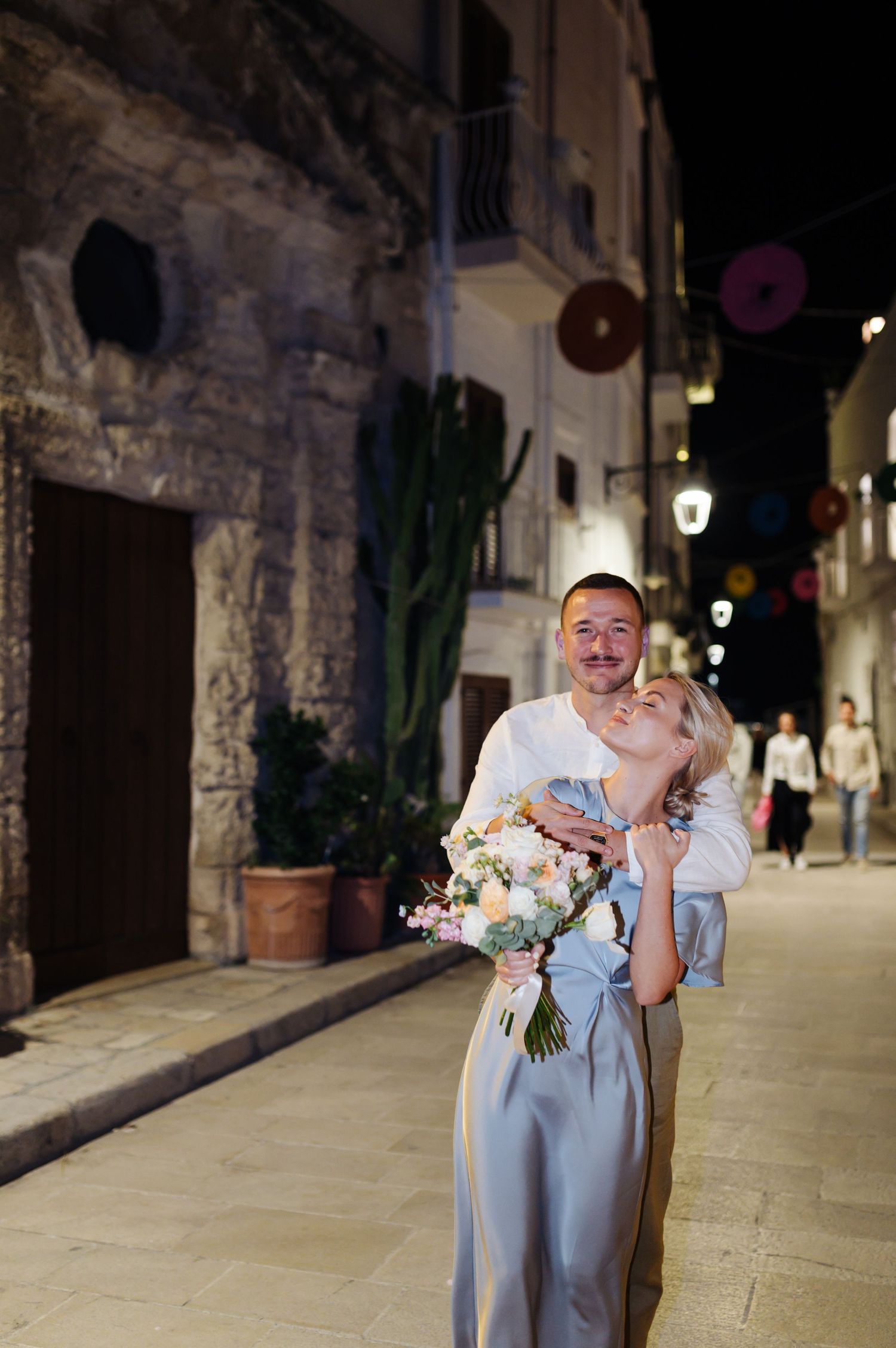 Wedding couple shares a romantic kiss on a charming European cobblestone street at night.