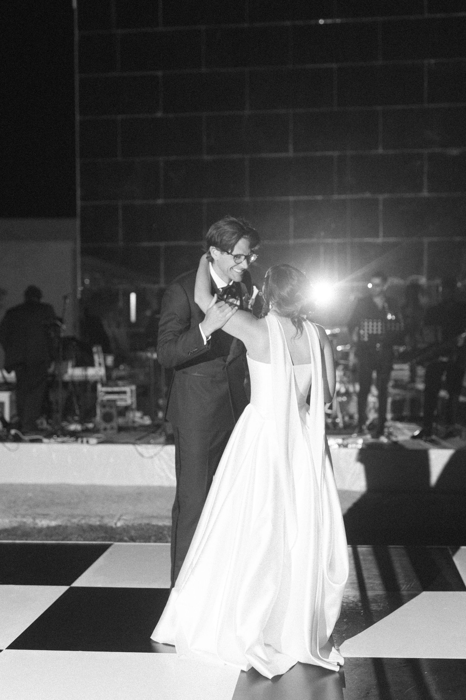 Black and white photo of bride and groom sharing their first dance on a checkered floor at wedding reception.