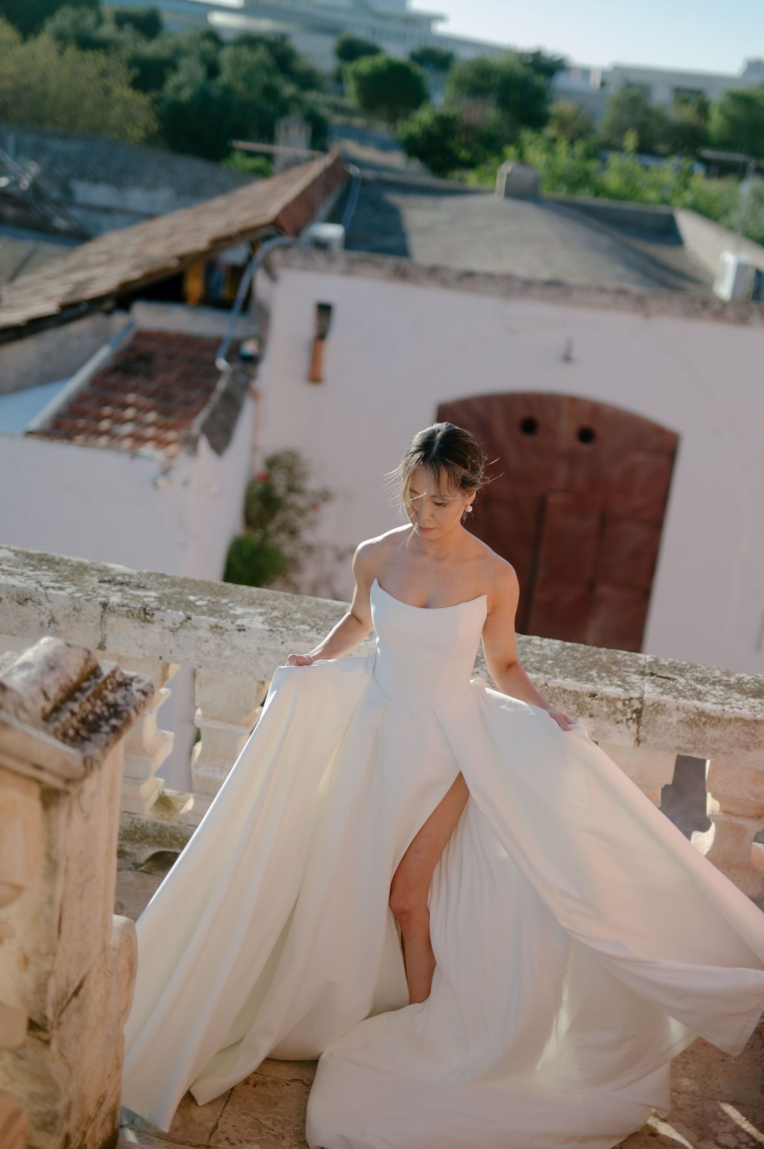 A flowing white wedding dress with a full skirt billows gracefully in the breeze against an outdoor backdrop.
