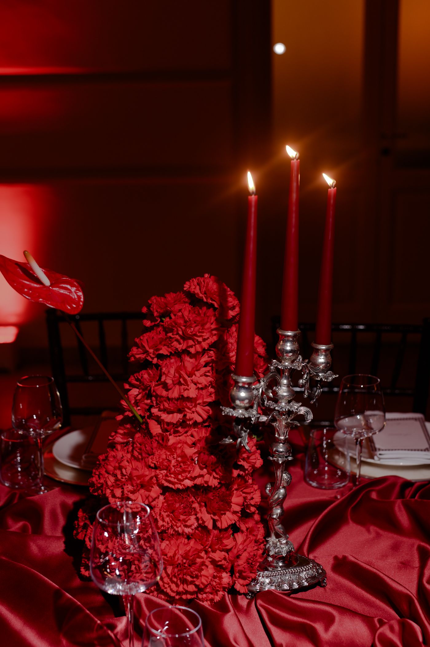 Red carnation centerpieces and silver candelabras create an elegant table setting with dramatic lighting.