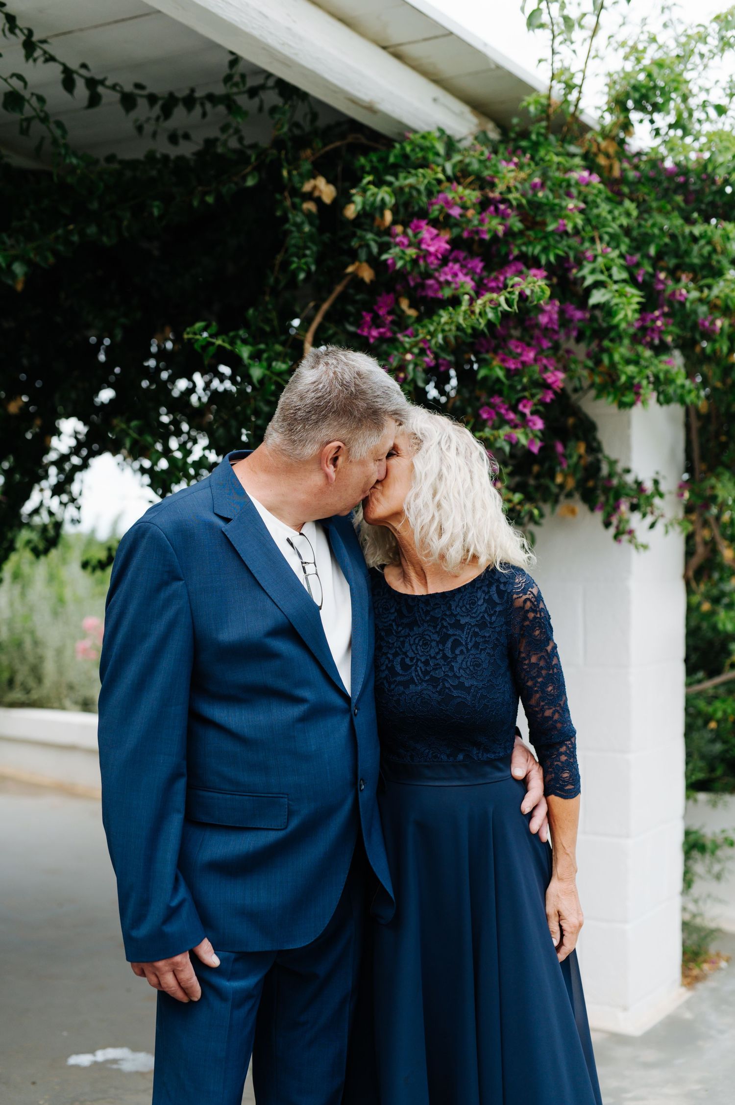 Couple in formal attire sharing an intimate moment under flowering bougainvillea.
